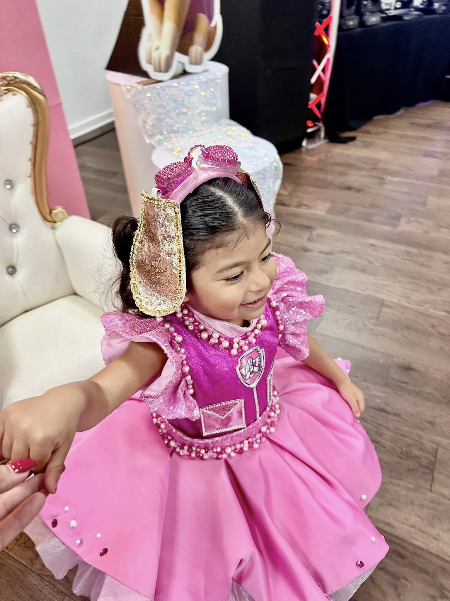 Young girl smiling while wearing a pink Paw Patrol themed dress and sparkly pup ear headband