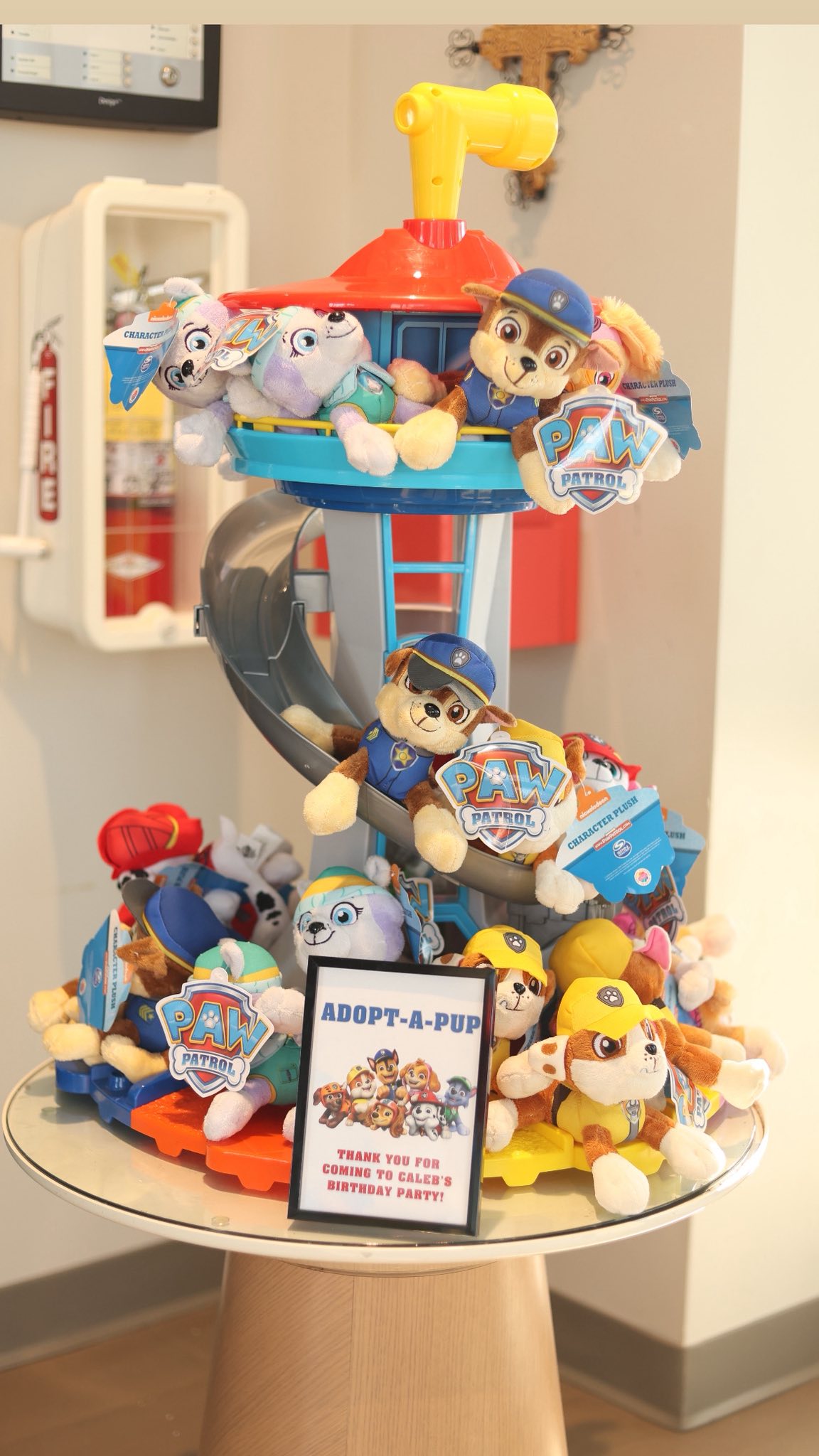 Paw Patrol tower display filled with plush character toys and an Adopt-a-Pup sign for a birthday party