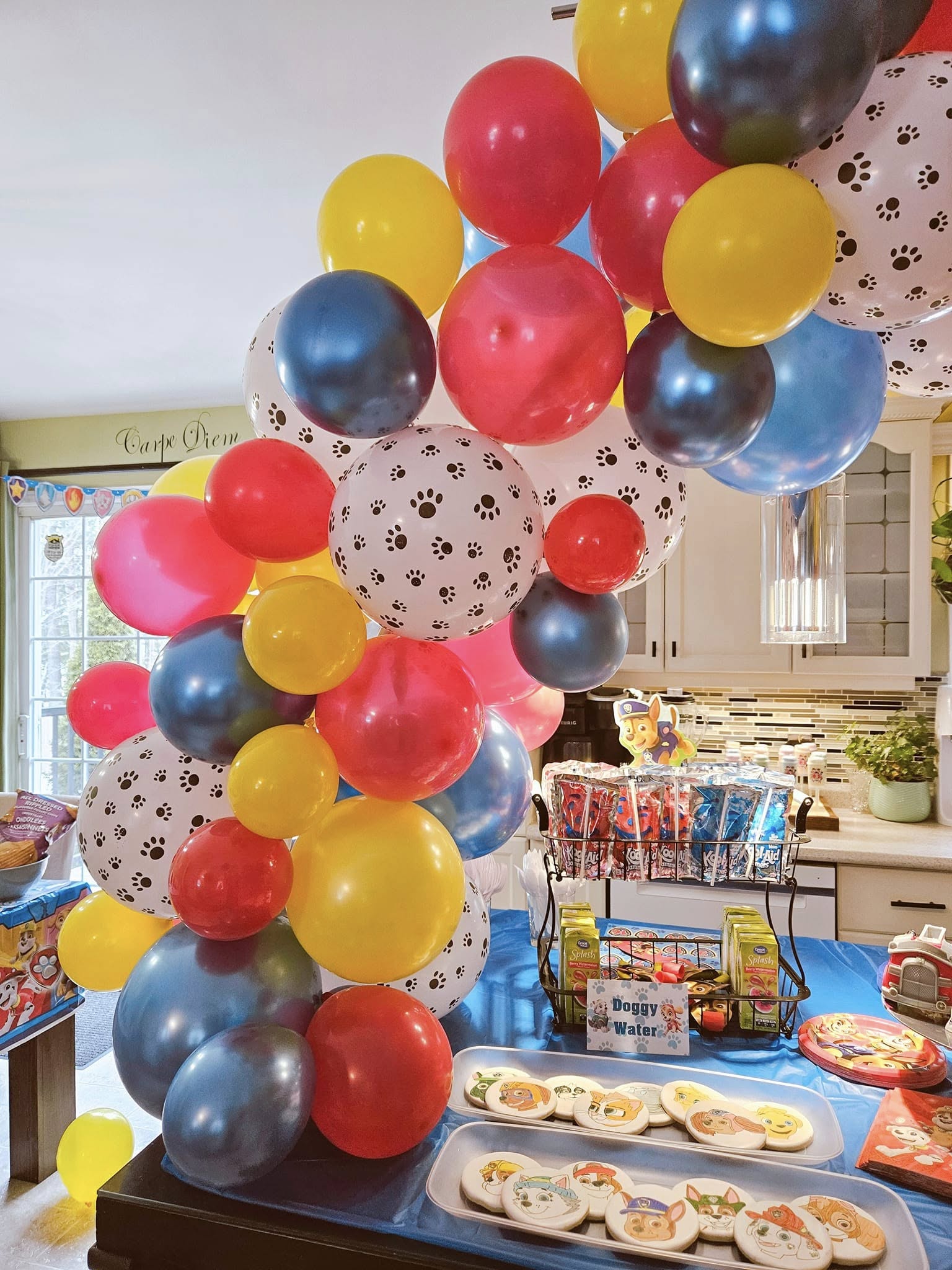 Colorful Paw Patrol themed balloon arch over a party table with decorated cookies and juice drinks.
