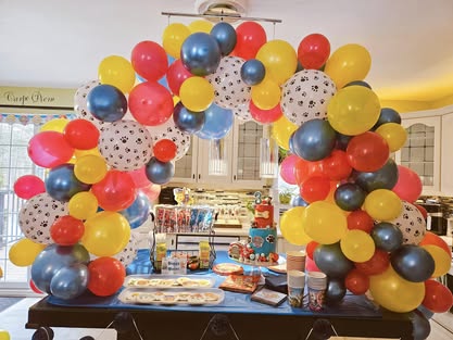Paw Patrol themed birthday party table with a balloon arch in red, yellow, and blue, and paw print balloons.