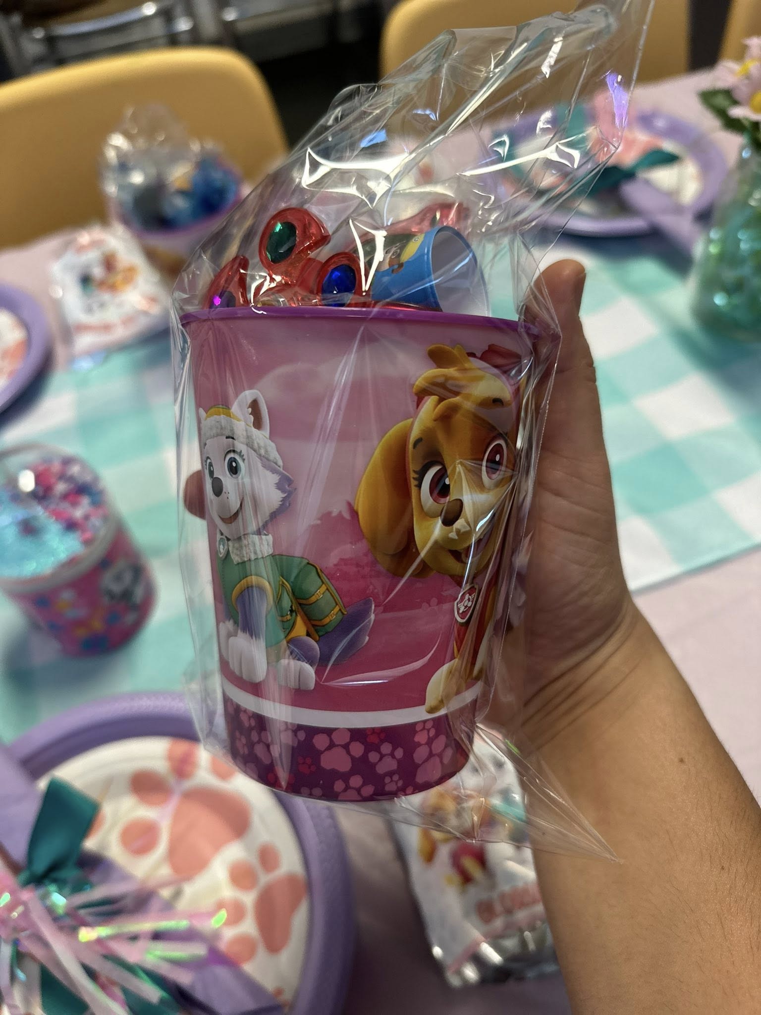 Hand holding a pink Paw Patrol party favor cup filled with small toys and wrapped in clear plastic.