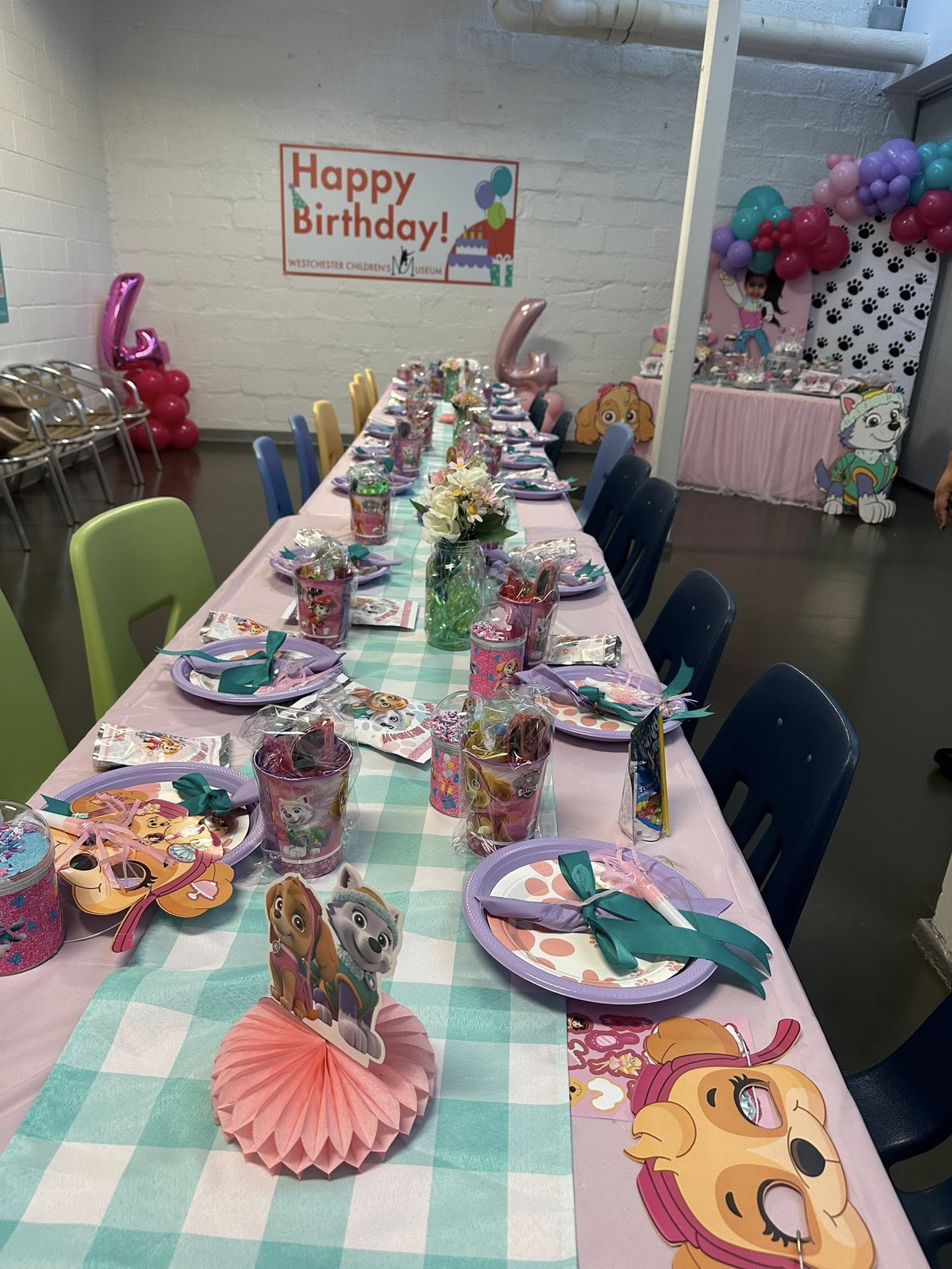 Paw Patrol themed event table with pink and teal decor, place settings, and party favors at Westchester Children's Museum.