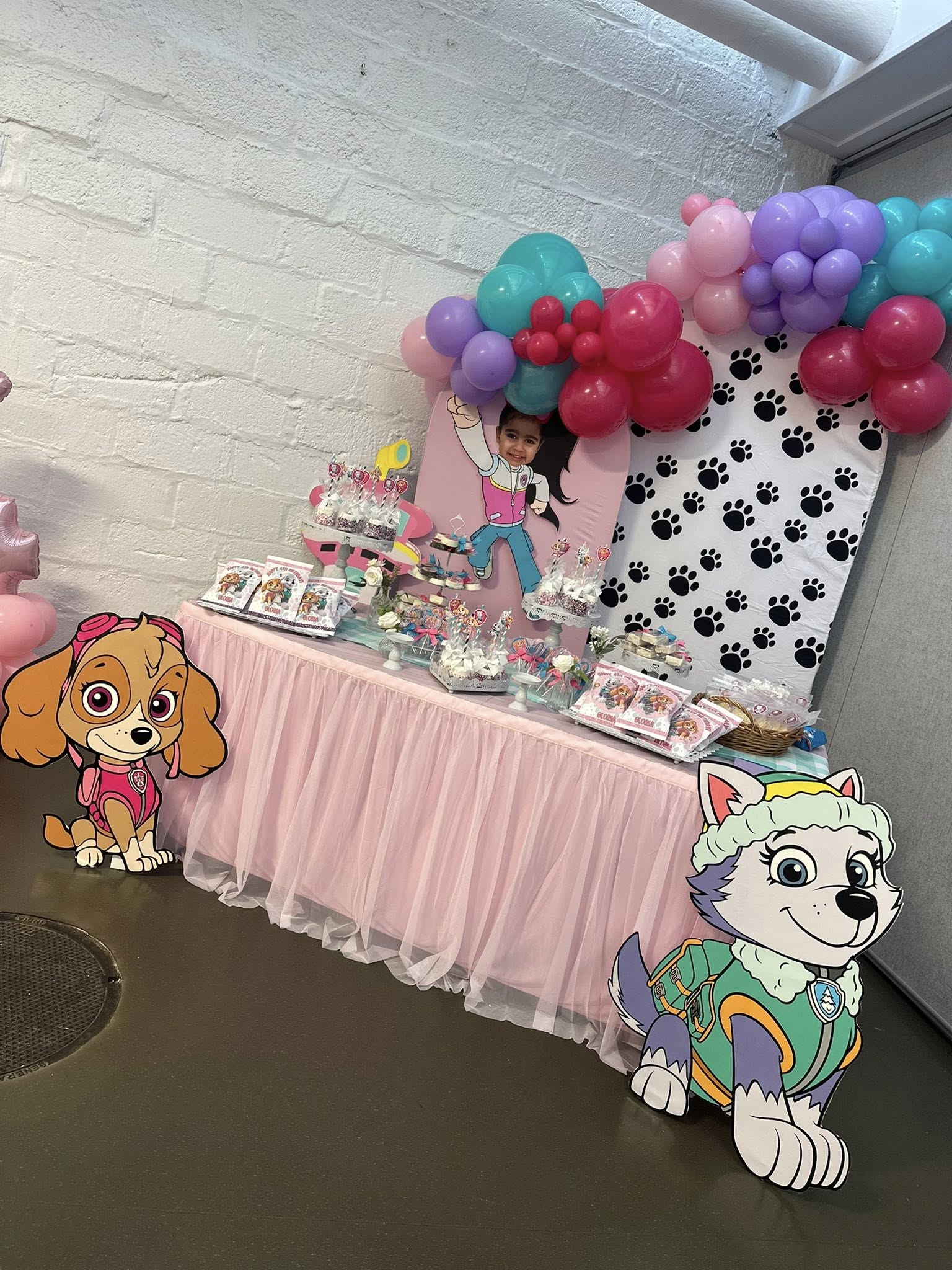 Paw Patrol themed party display table with pink tutu skirt, character cutouts, and balloon arch.