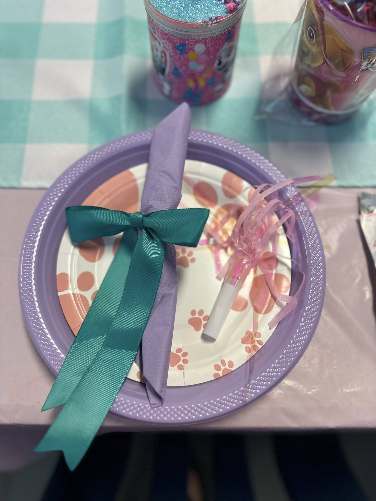 Place setting with a purple plate, paw print design, wrapped napkin with teal ribbon, and a party blower.