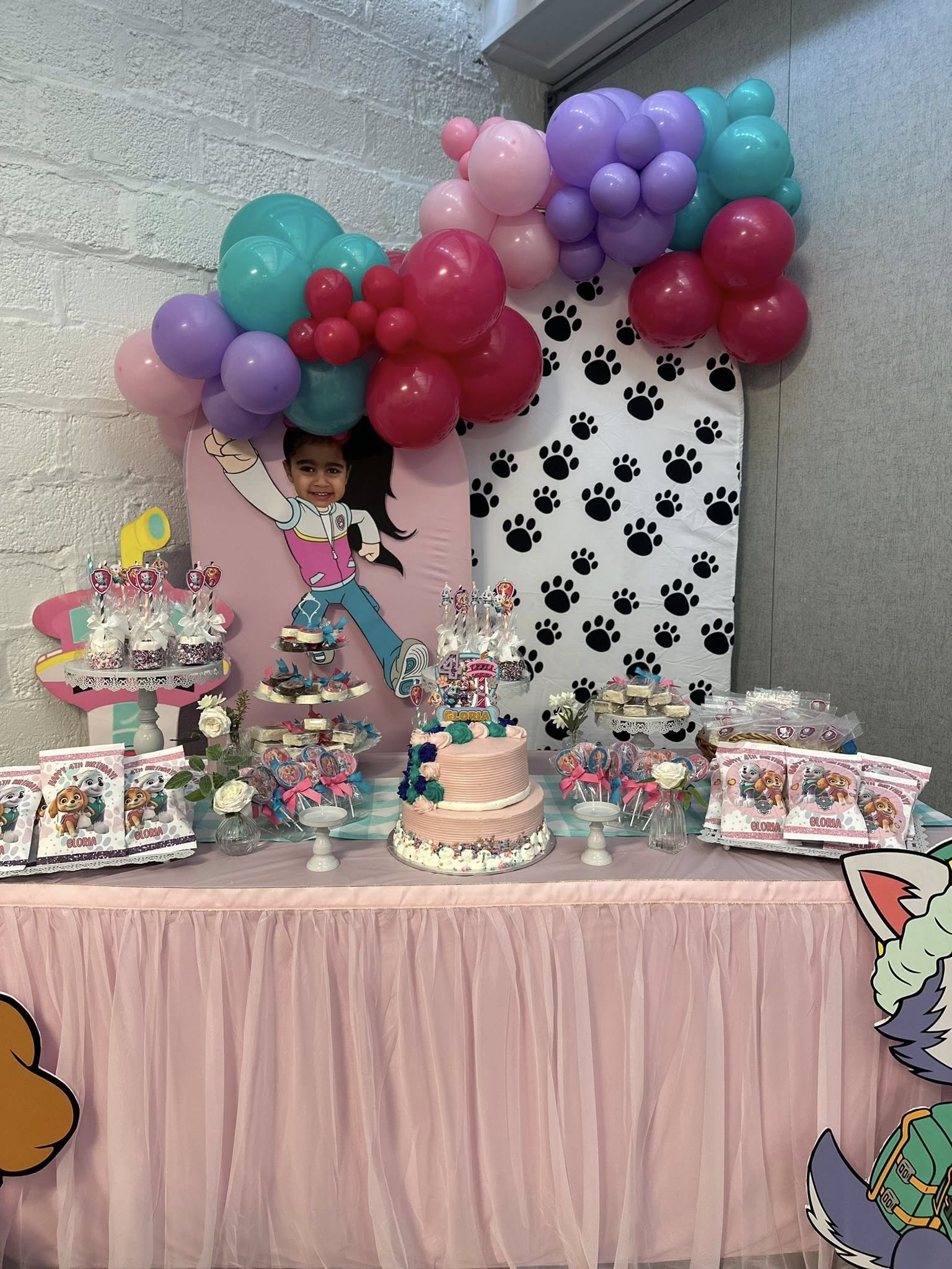 Paw Patrol themed 4th birthday dessert table with a tiered cake, party favors, and colorful balloon arch.