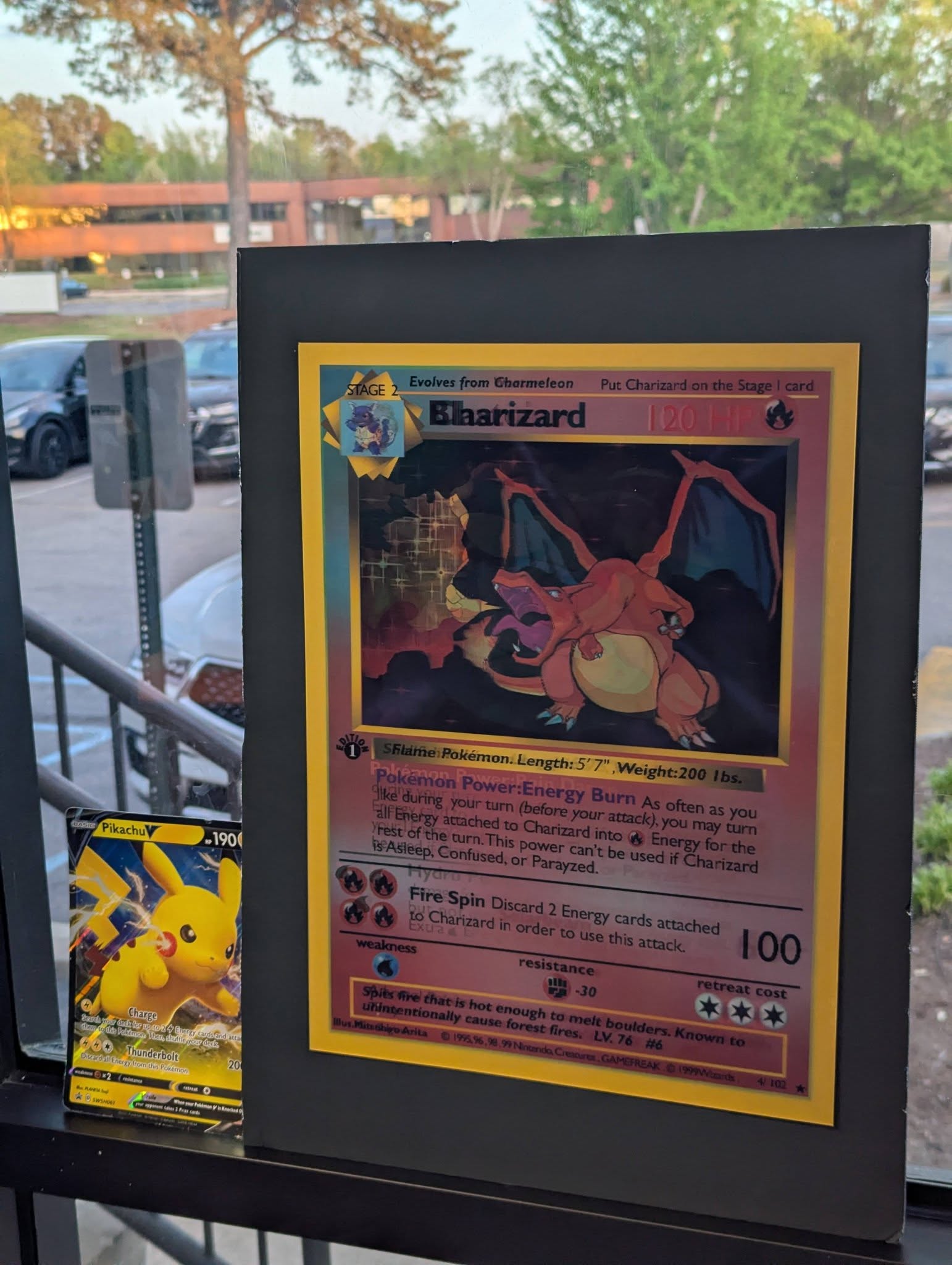 Framed Charizard holographic Pokemon card displayed next to a Pikachu V card on a window sill.