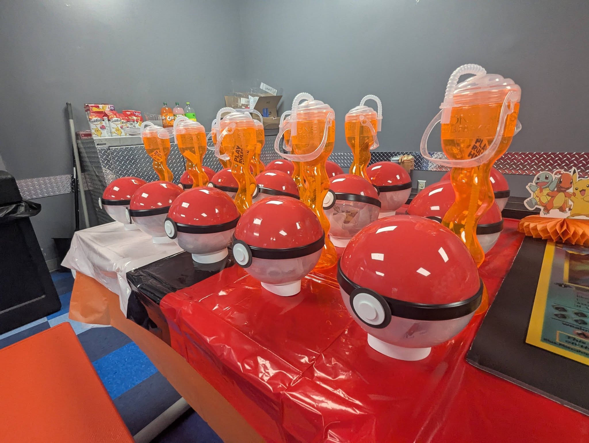 Table set with red and white Poke Ball drink containers and orange beverage cups for a Pokemon themed party