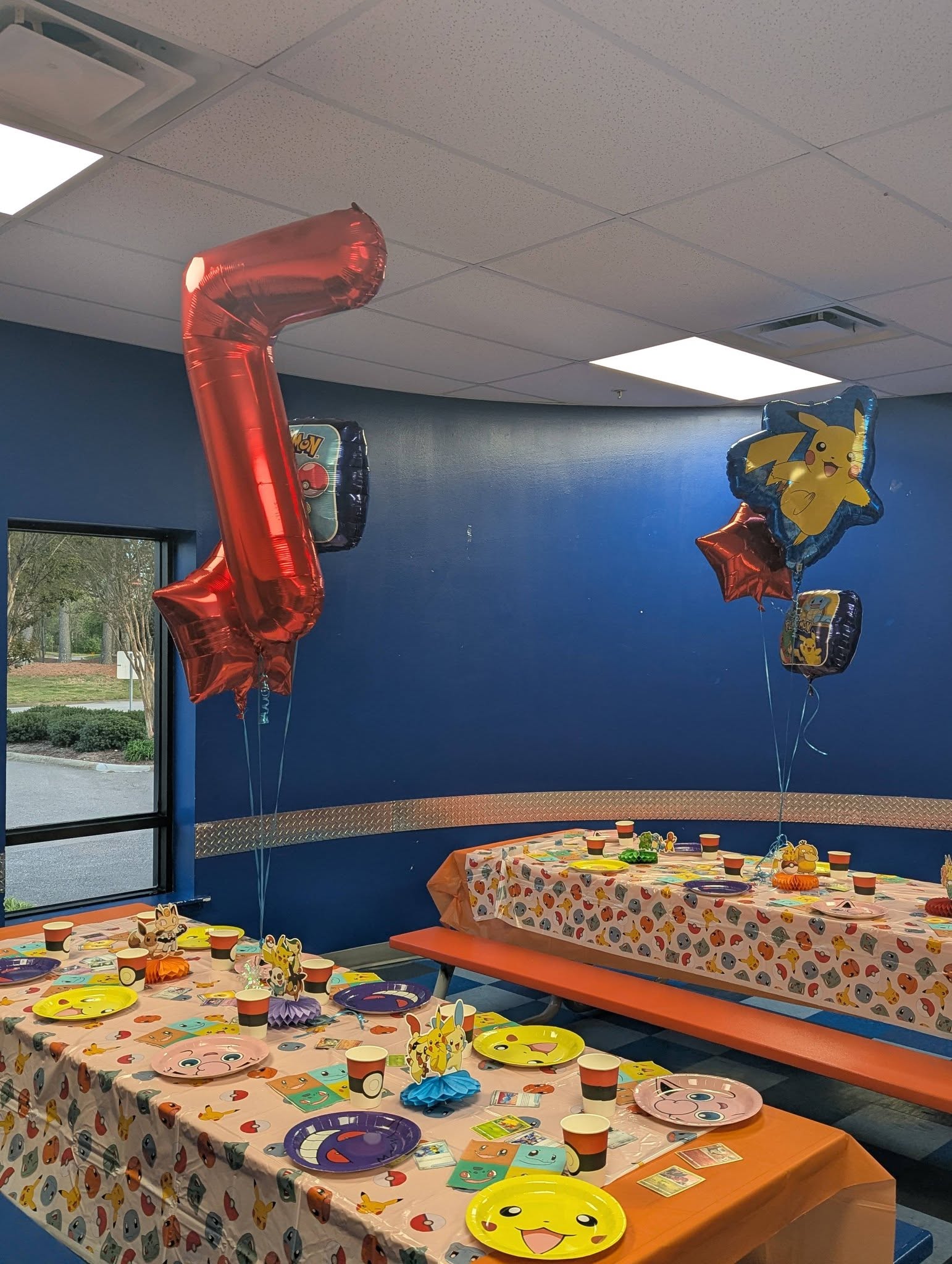 Pokemon themed birthday party table setting with plates, cups, and Pikachu foil balloons.