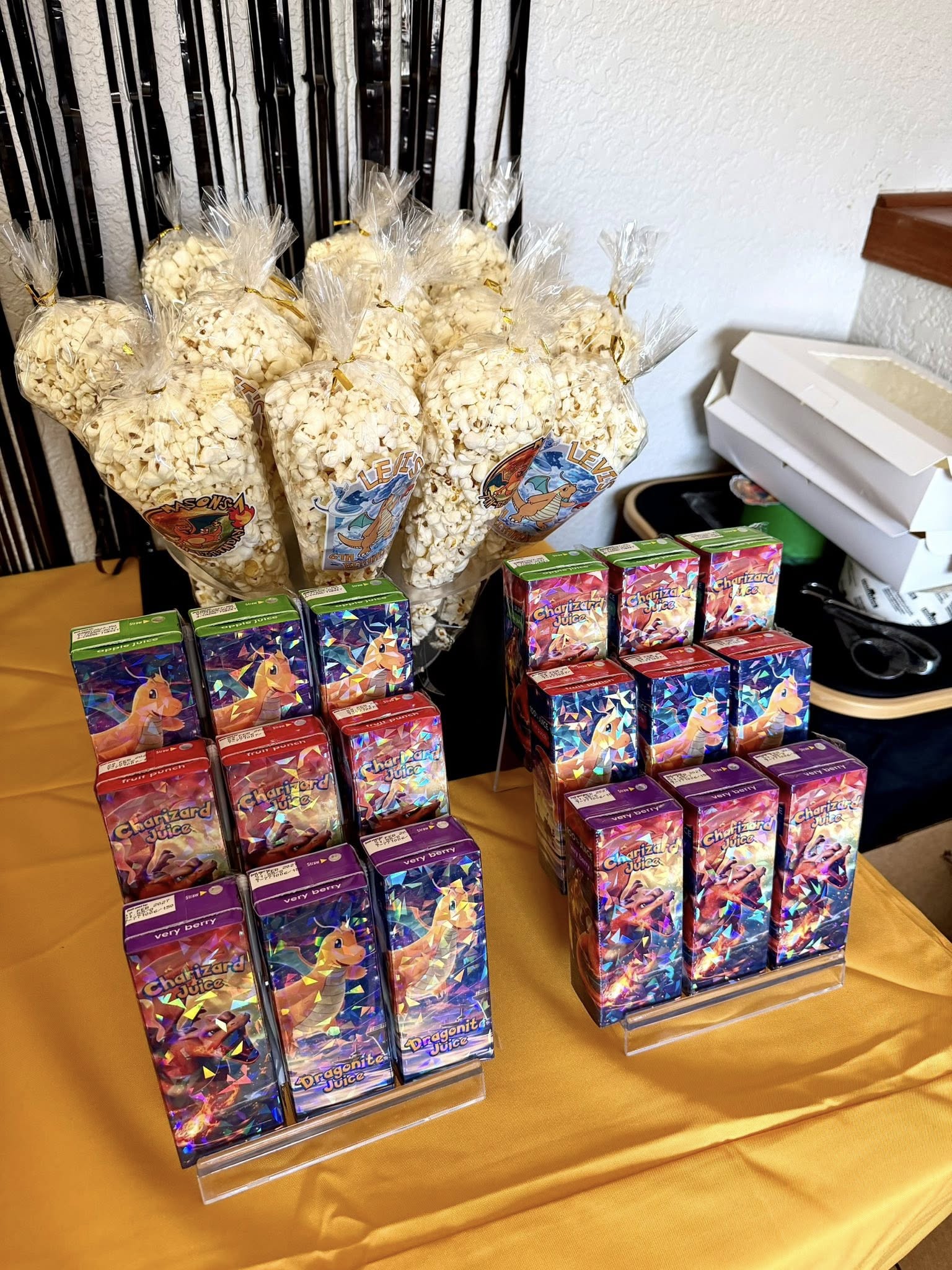 Popcorn cones alongside Pokémon-themed juice boxes on a yellow tablecloth.