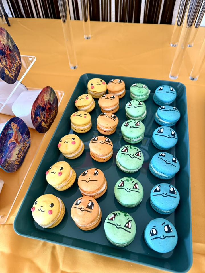 Tray of assorted Pokemon character-themed macarons including Pikachu, Charmander, Bulbasaur, and Squirtle designs.