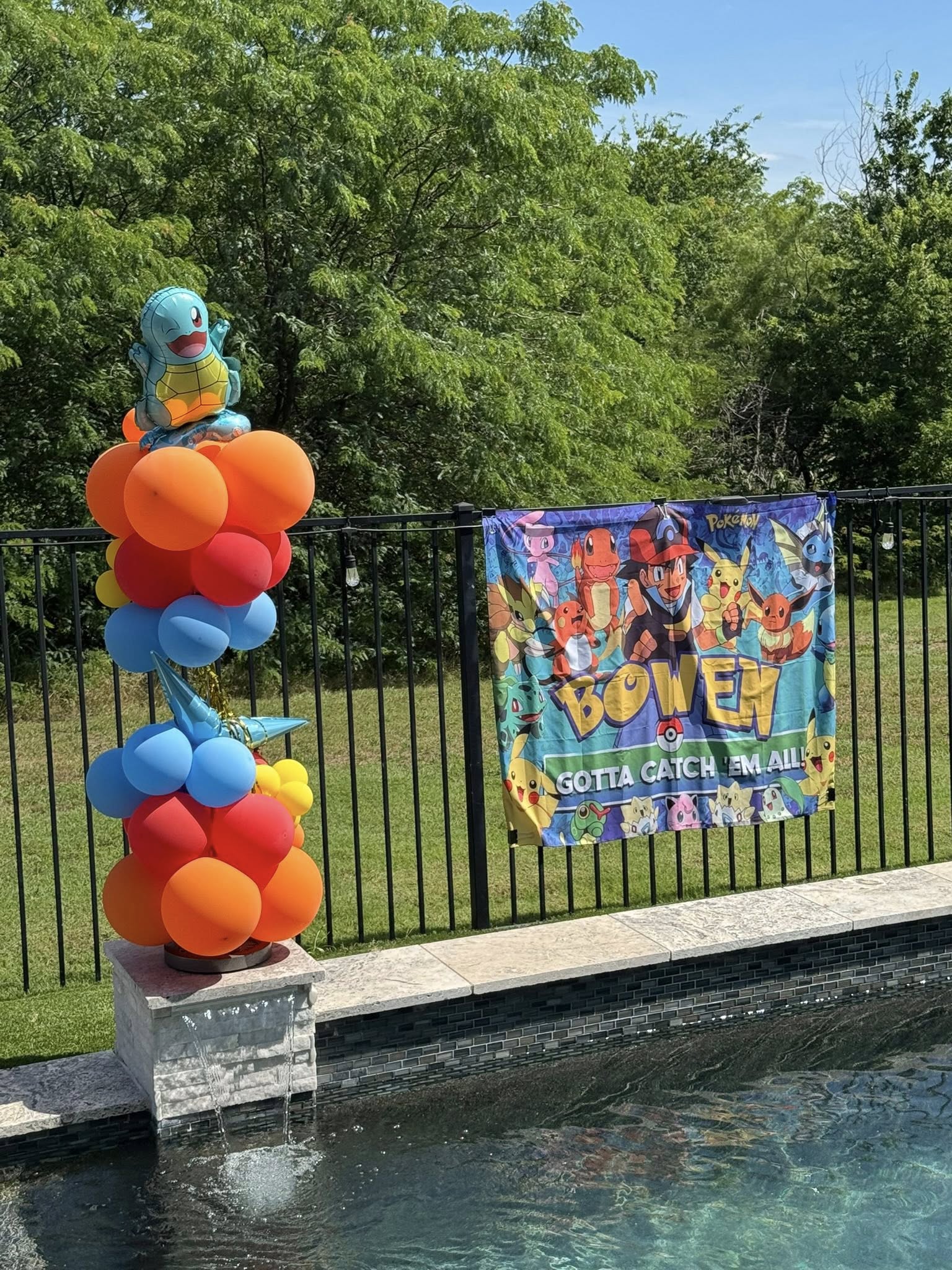 Pokemon themed birthday party decorations with a Squirtle balloon arch and a personalized banner by a pool