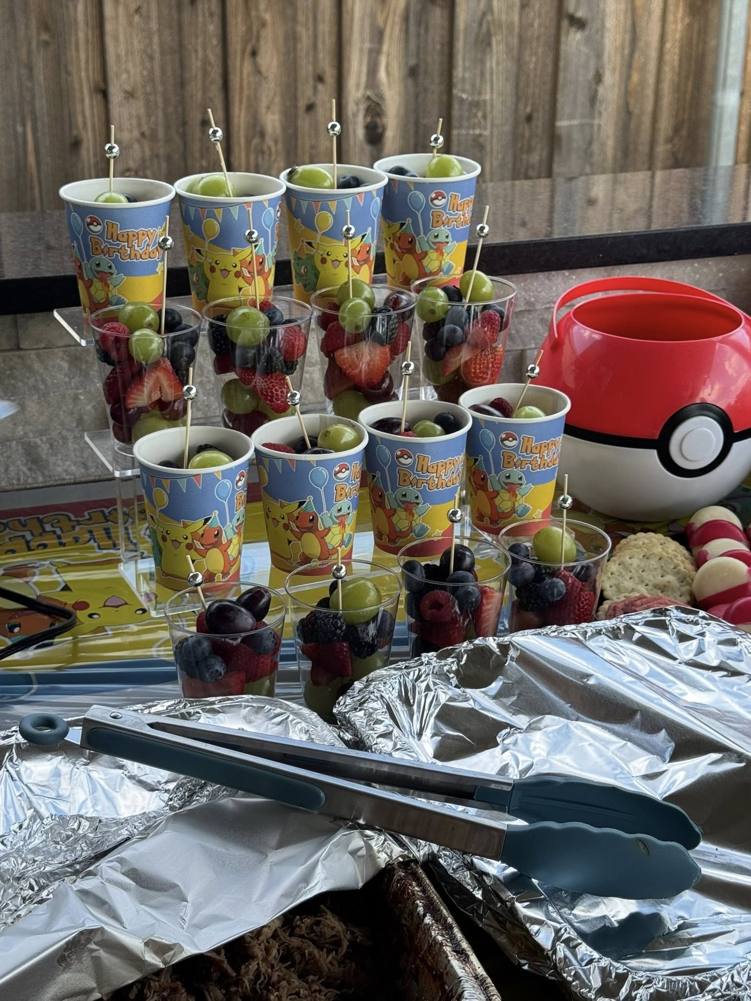 Pokemon themed fruit cups for a birthday party arranged on a serving stand with a red Pokeball snack bucket