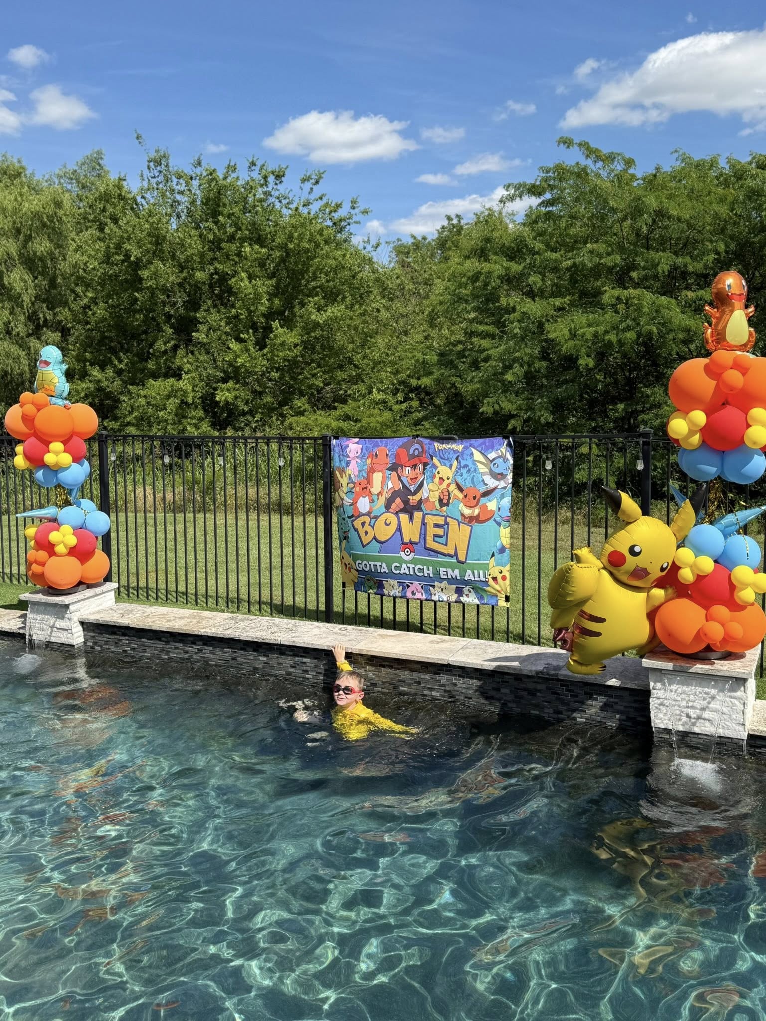 Child swimming at a pool party featuring a Pokemon banner and colorful themed balloon decorations.