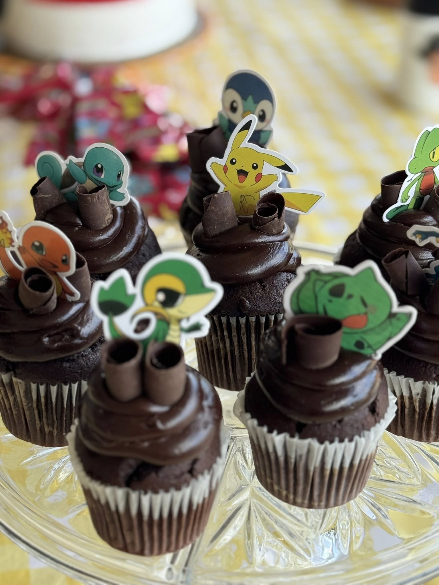 Group of chocolate cupcakes topped with chocolate curls and various Pokemon character cupcake toppers.