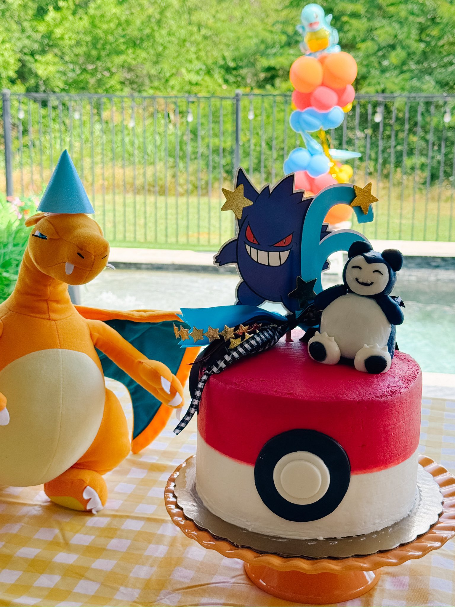 Pokemon themed birthday cake shaped like a Poke Ball with Gengar and Snorlax toppers next to a Charizard plush