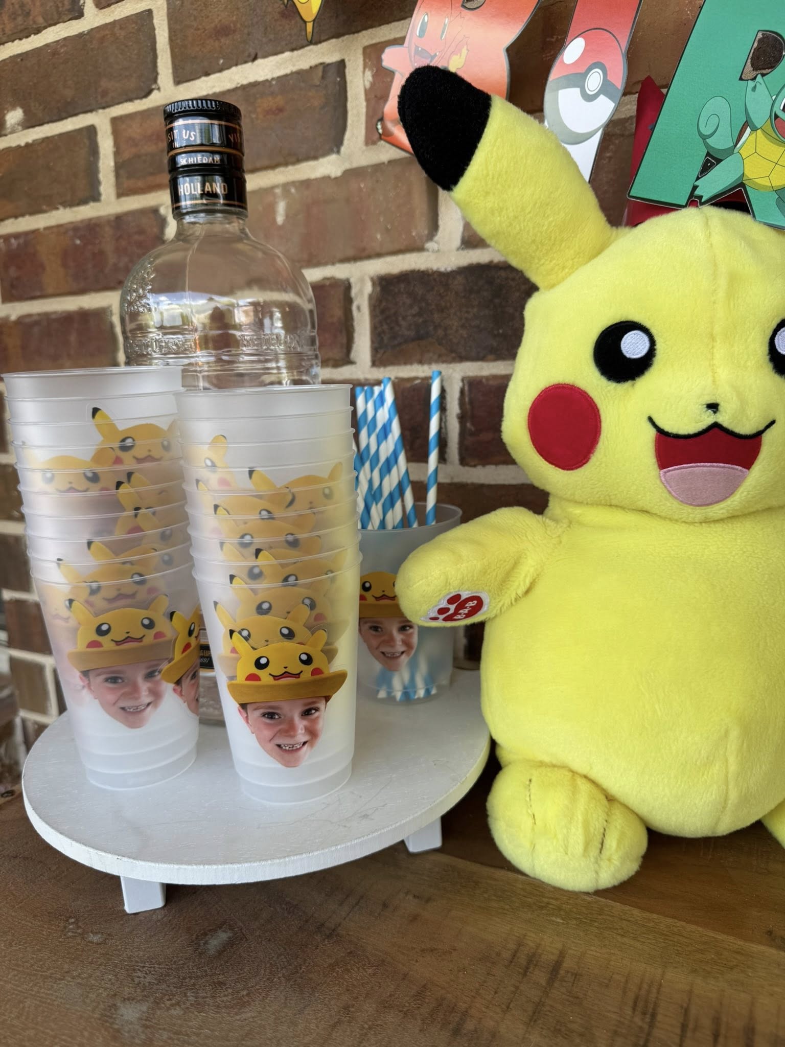 Custom clear cups featuring child's photo wearing a Pikachu hat next to a plush Pikachu toy.