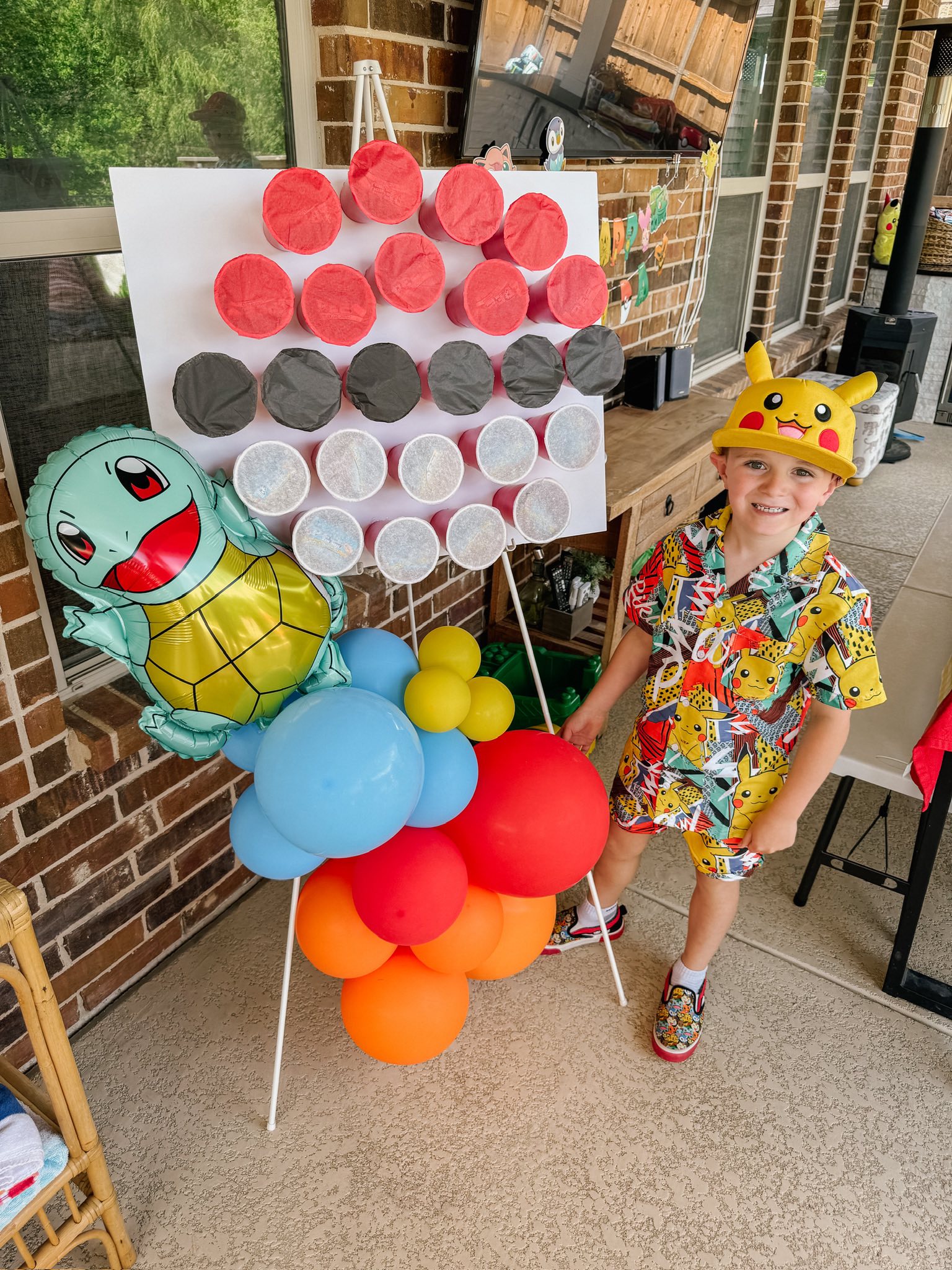 Young boy wearing a Pikachu hat and shirt standing next to a DIY Pokemon-themed cup-punch party game board