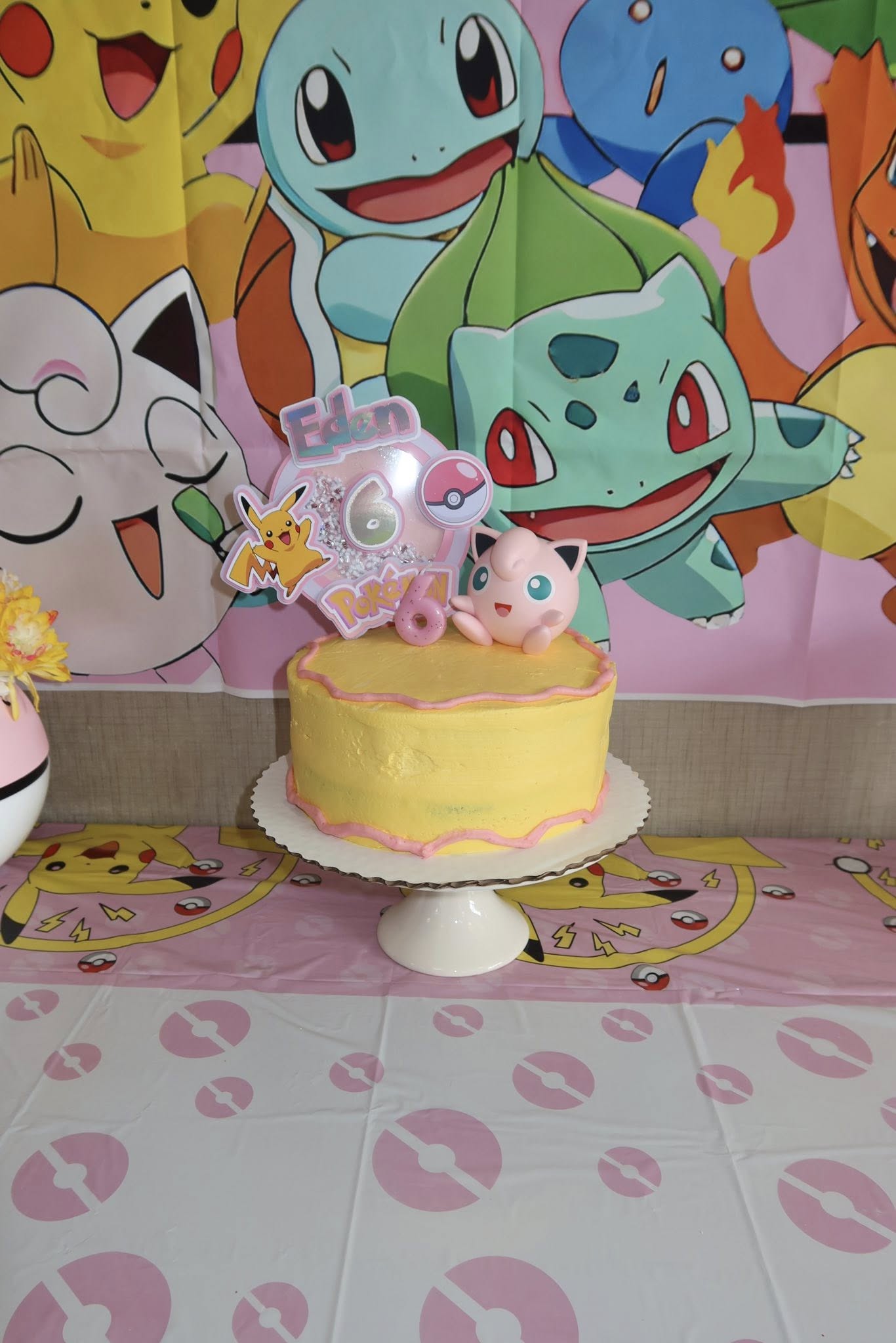 Yellow Pokemon birthday cake with a glittery number six topper, Pikachu and Jigglypuff accents, and party decor.