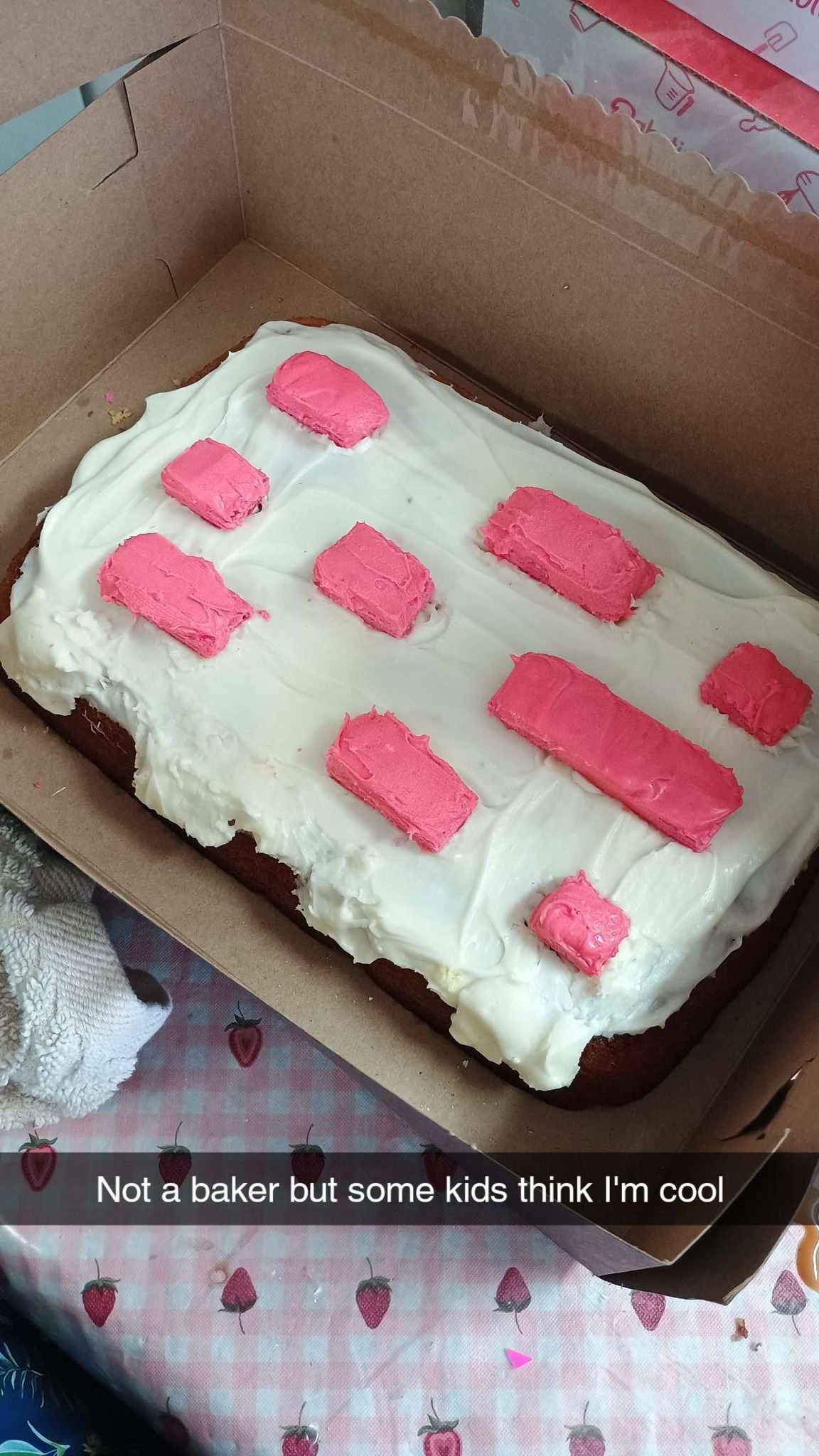 Rectangular sheet cake with white frosting and pink rectangular icing accents in a cardboard box.