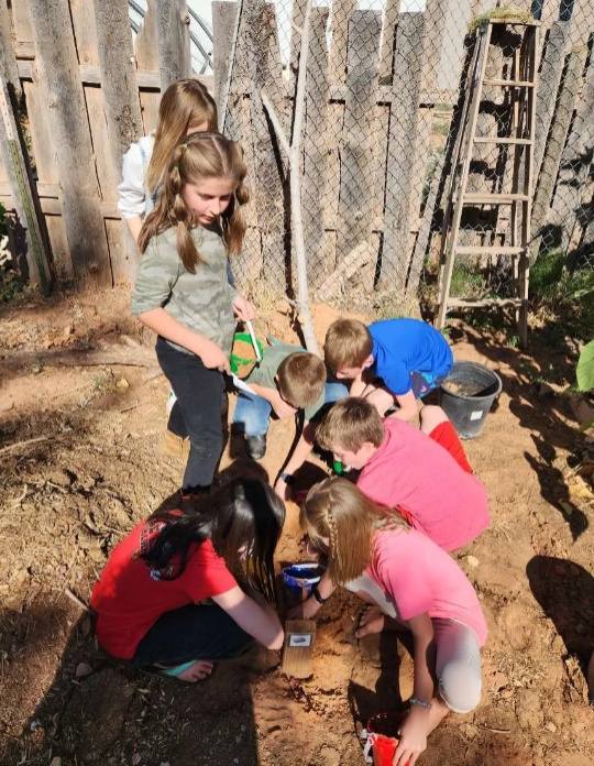 Group of children gardening and digging in the soil outdoors by a wooden fence