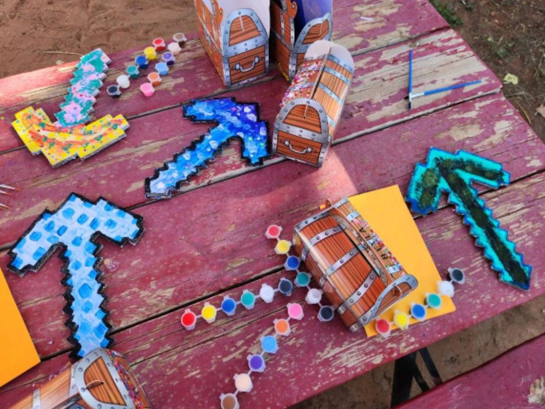 DIY treasure chest craft kit with cardboard boxes, pixelated pickaxes, and paint sets on a picnic table