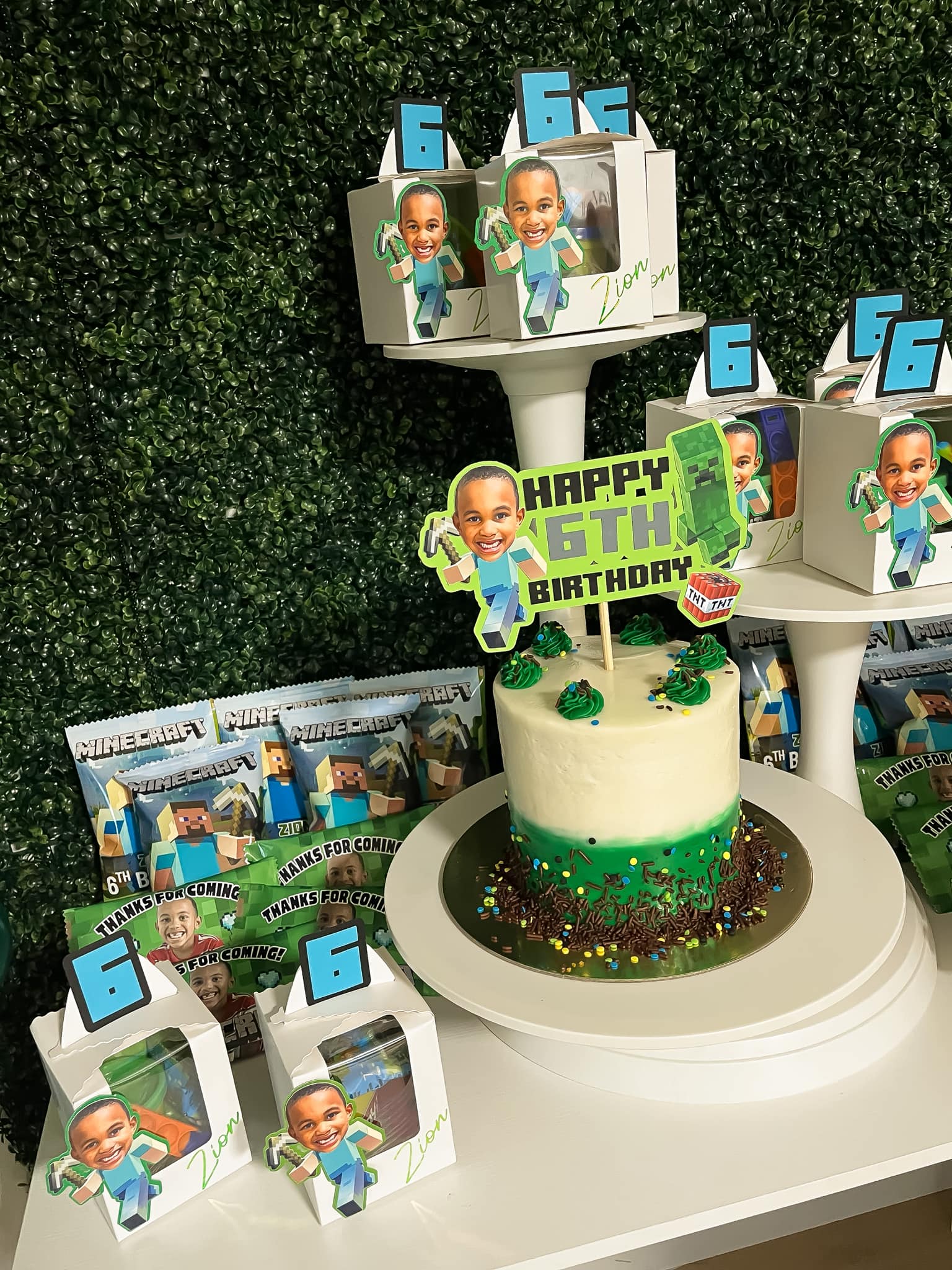 Minecraft-themed 6th birthday cake surrounded by personalized treat boxes with child's photo
