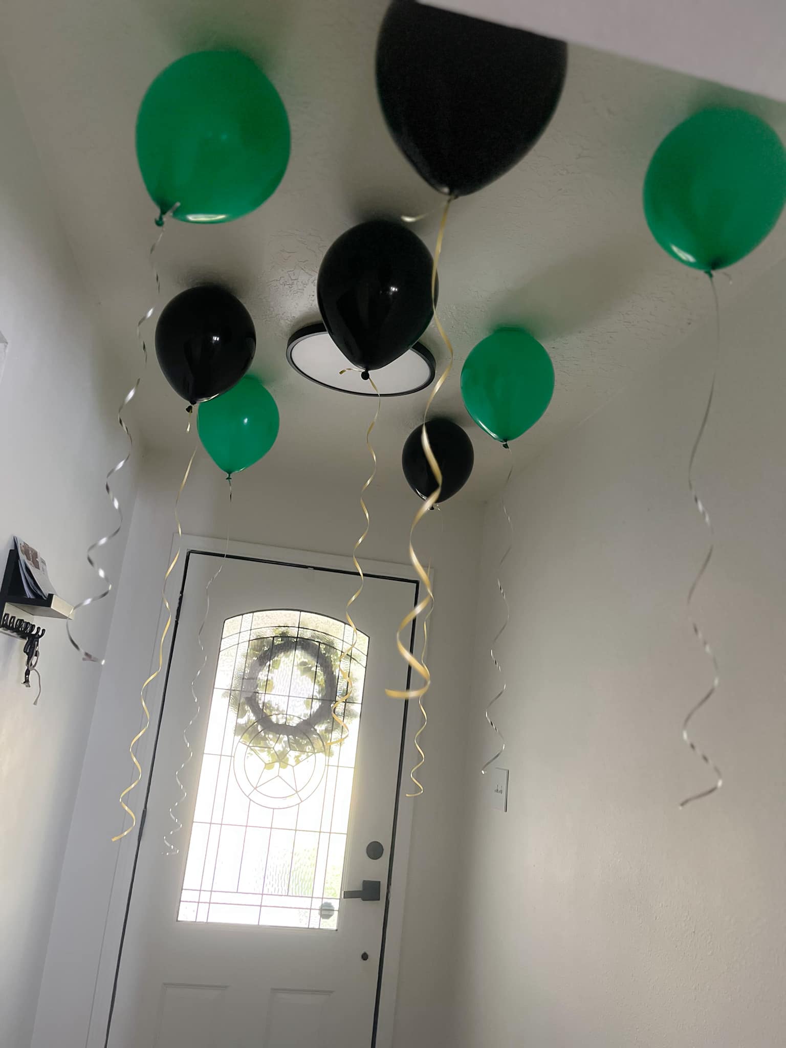Black and green balloons with gold ribbons floating near an entry door