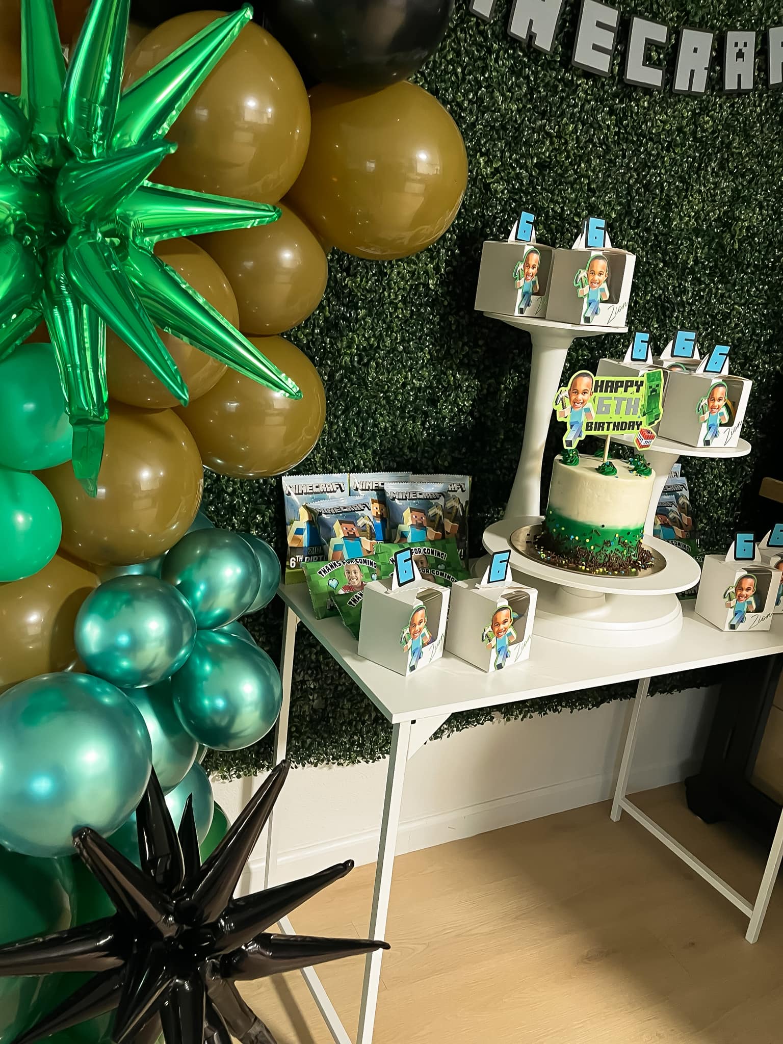 Minecraft themed 6th birthday dessert table featuring a decorated cake, party favor boxes, and green and gold balloons