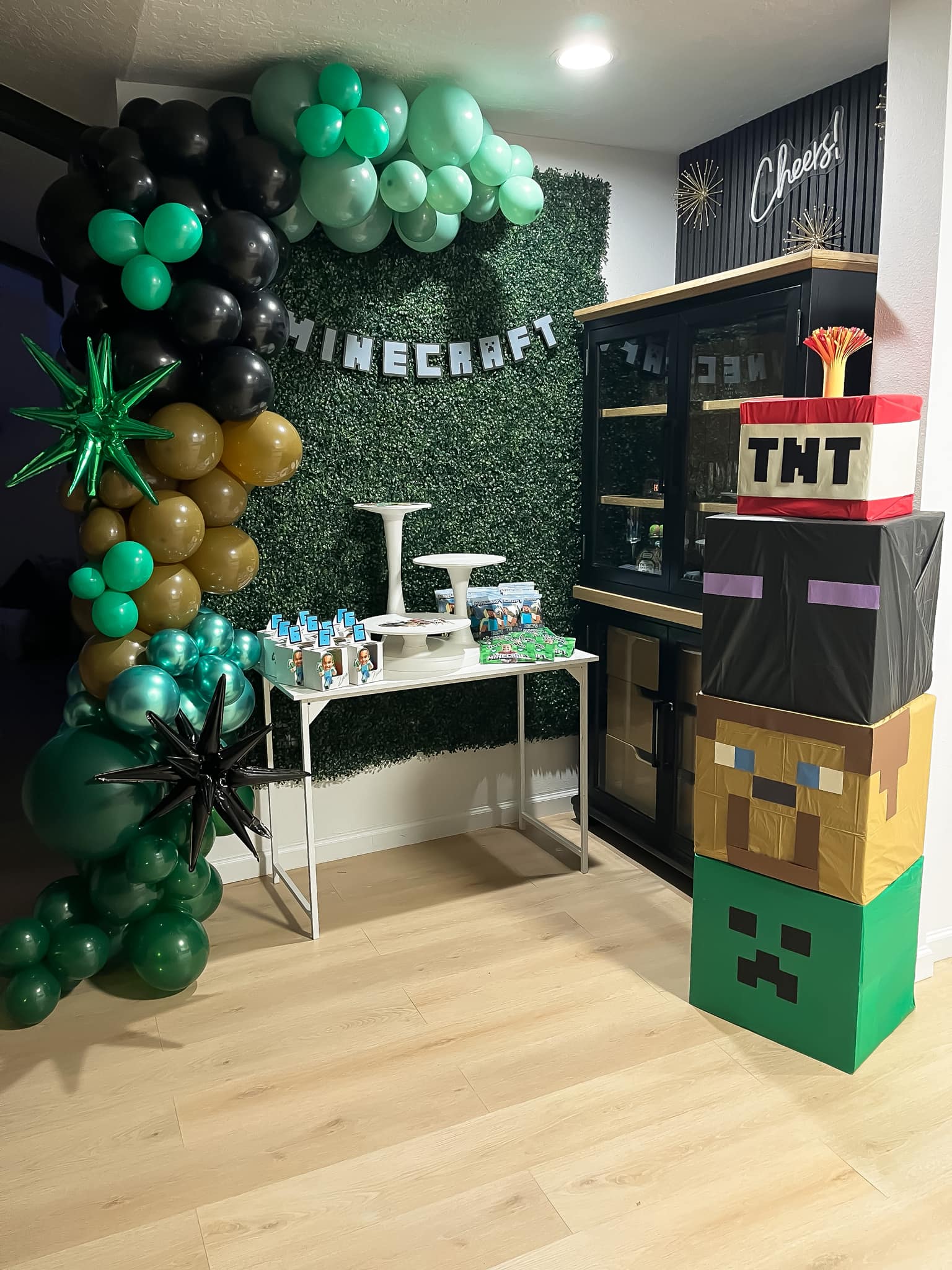 Minecraft themed birthday party dessert table with a balloon arch and stacked cardboard block characters.
