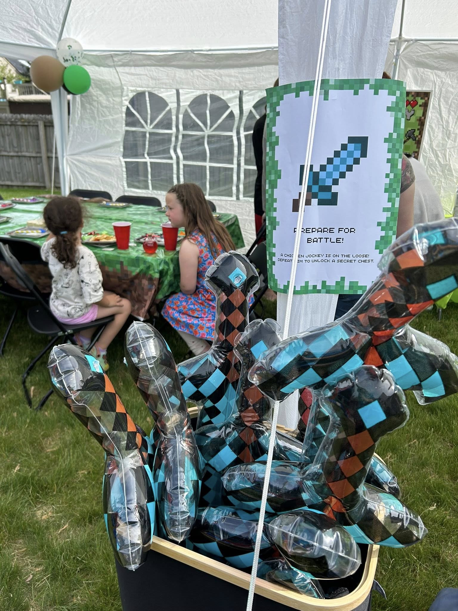 Inflatable Minecraft-style pixelated diamond swords in a basket next to a Prepare for Battle party sign.