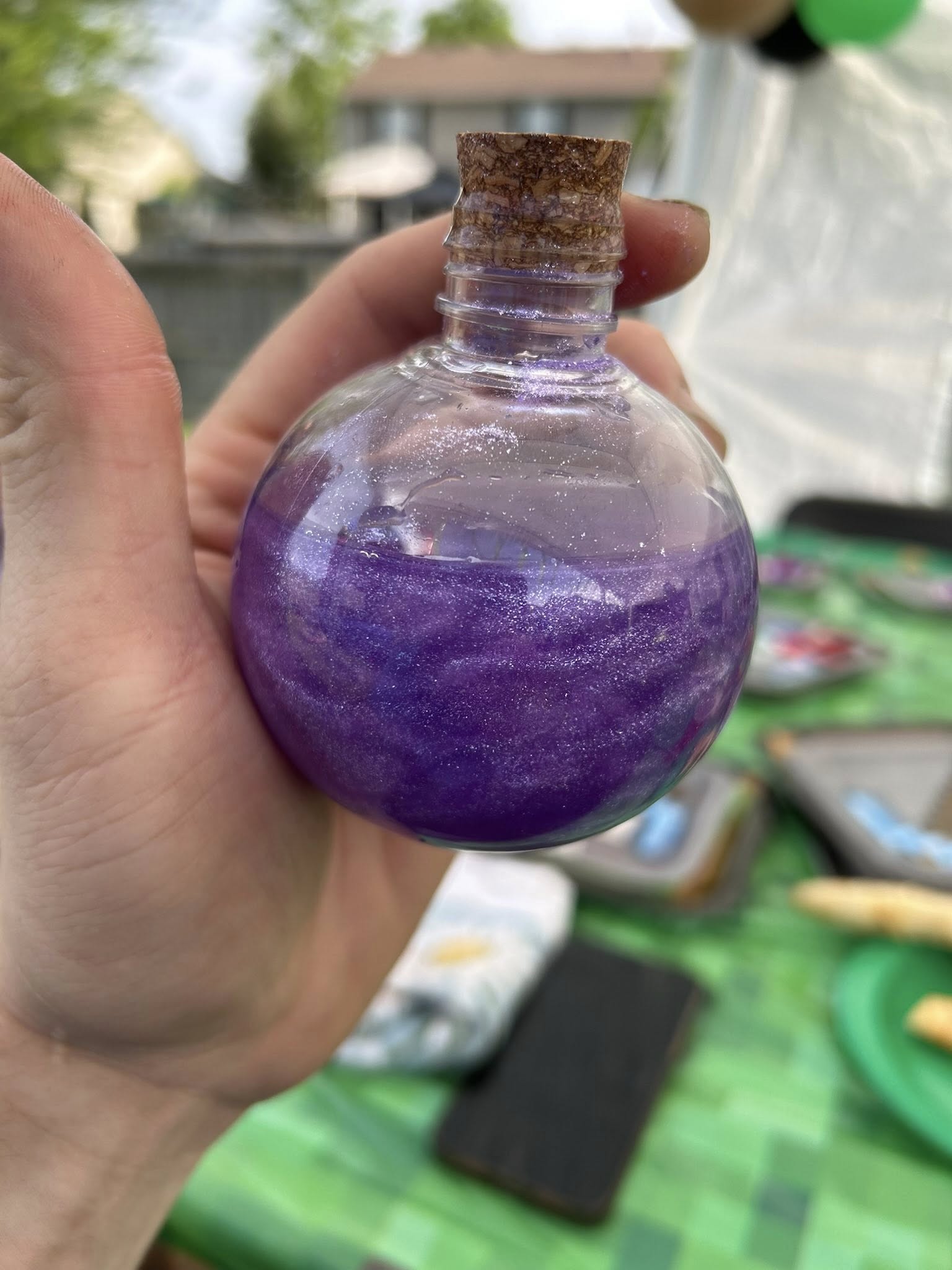 Round glass bottle with a cork stopper containing swirling purple glitter liquid