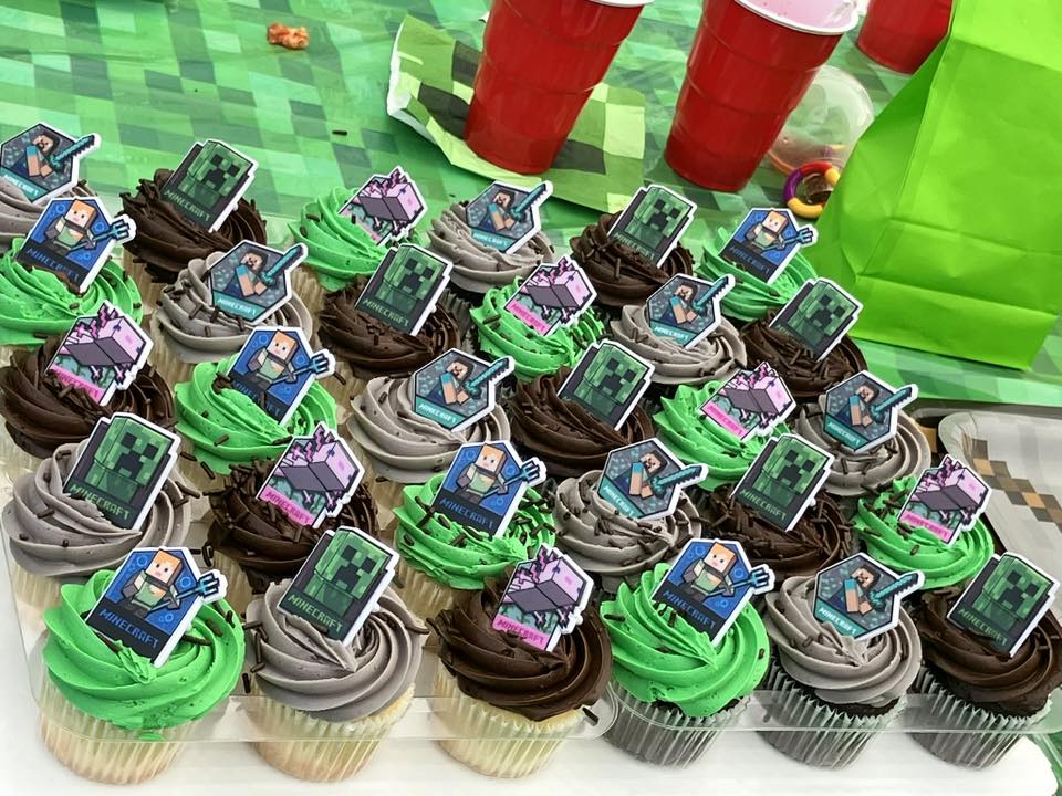 Cupcakes decorated with Minecraft themed toppers including characters and green frosting on a party table