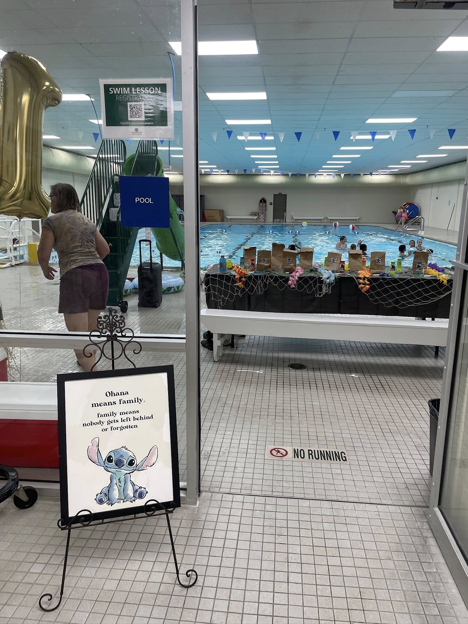 Indoor pool area decorated for a Lilo and Stitch themed event with a framed sign and party favors on a table.