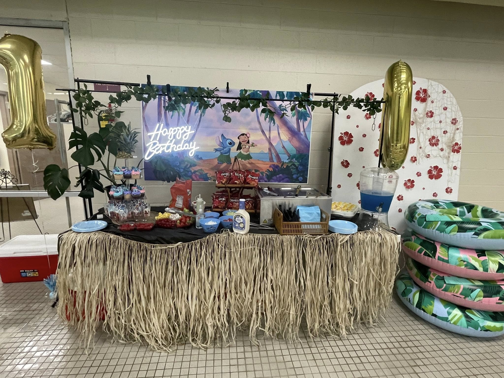 Lilo and Stitch themed birthday party food table with a grass skirt tablecloth, snacks, and tropical decorations.