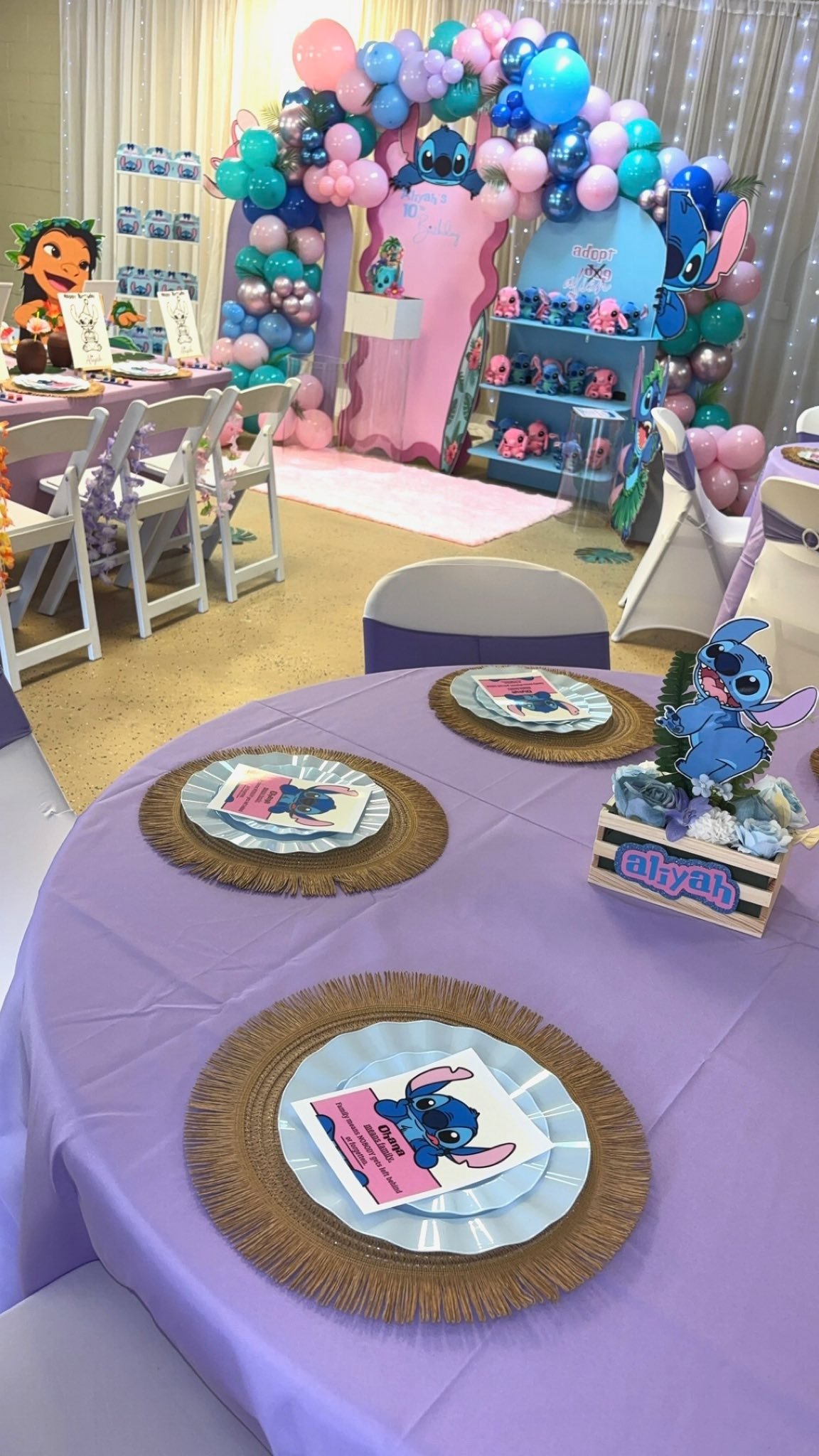 Stitch-themed birthday party setup with purple tablecloths, themed place settings, and balloon decorations.