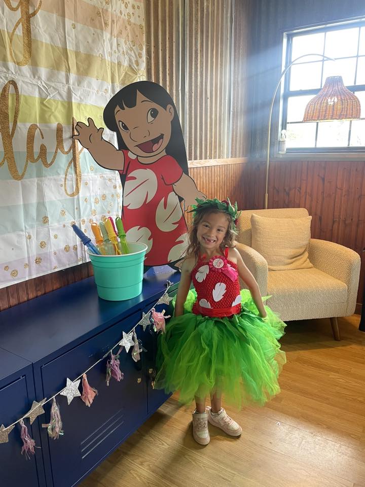 Young girl smiling while wearing a tropical leaf-themed tutu and matching headband at a party
