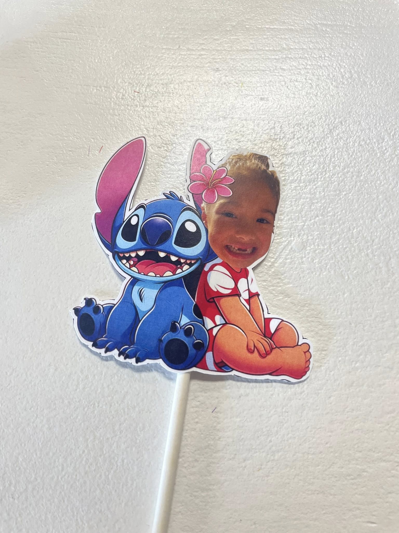 Custom cake topper featuring a cartoon Stitch sitting back-to-back with a photo of a young girl with a flower in her hair.