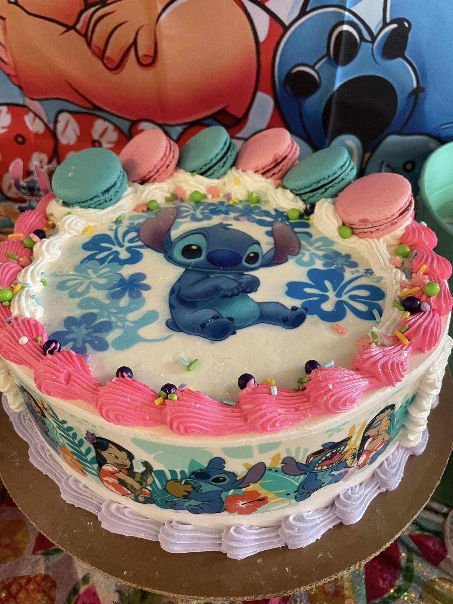 Stitch themed birthday cake decorated with pink frosting, colorful sprinkles, and blue and pink macarons.