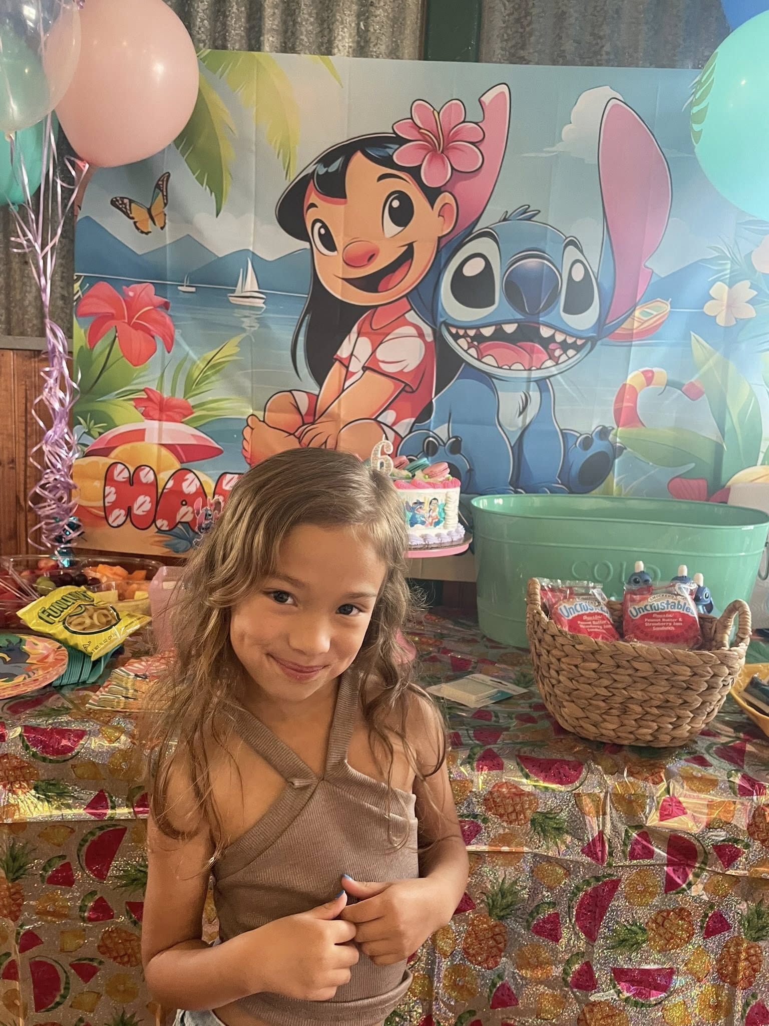 Young girl smiling in front of a Lilo and Stitch themed birthday party backdrop and table.