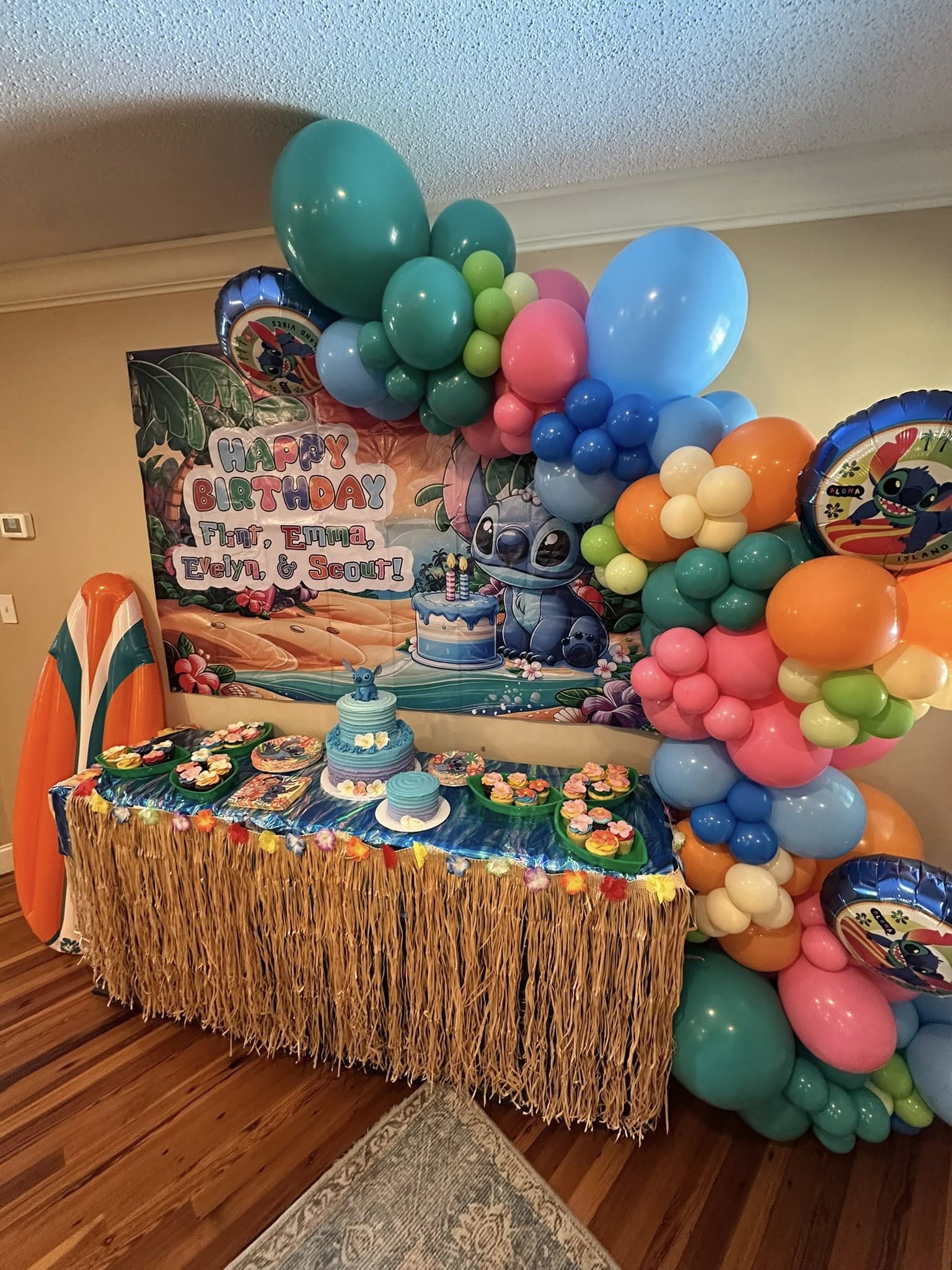 Stitch themed birthday party display with a tropical backdrop, cupcake table, and colorful balloon arch.