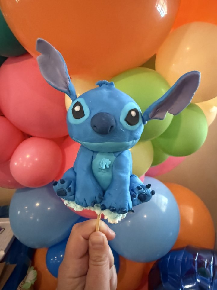 Stitch character cake pop held against a colorful balloon backdrop