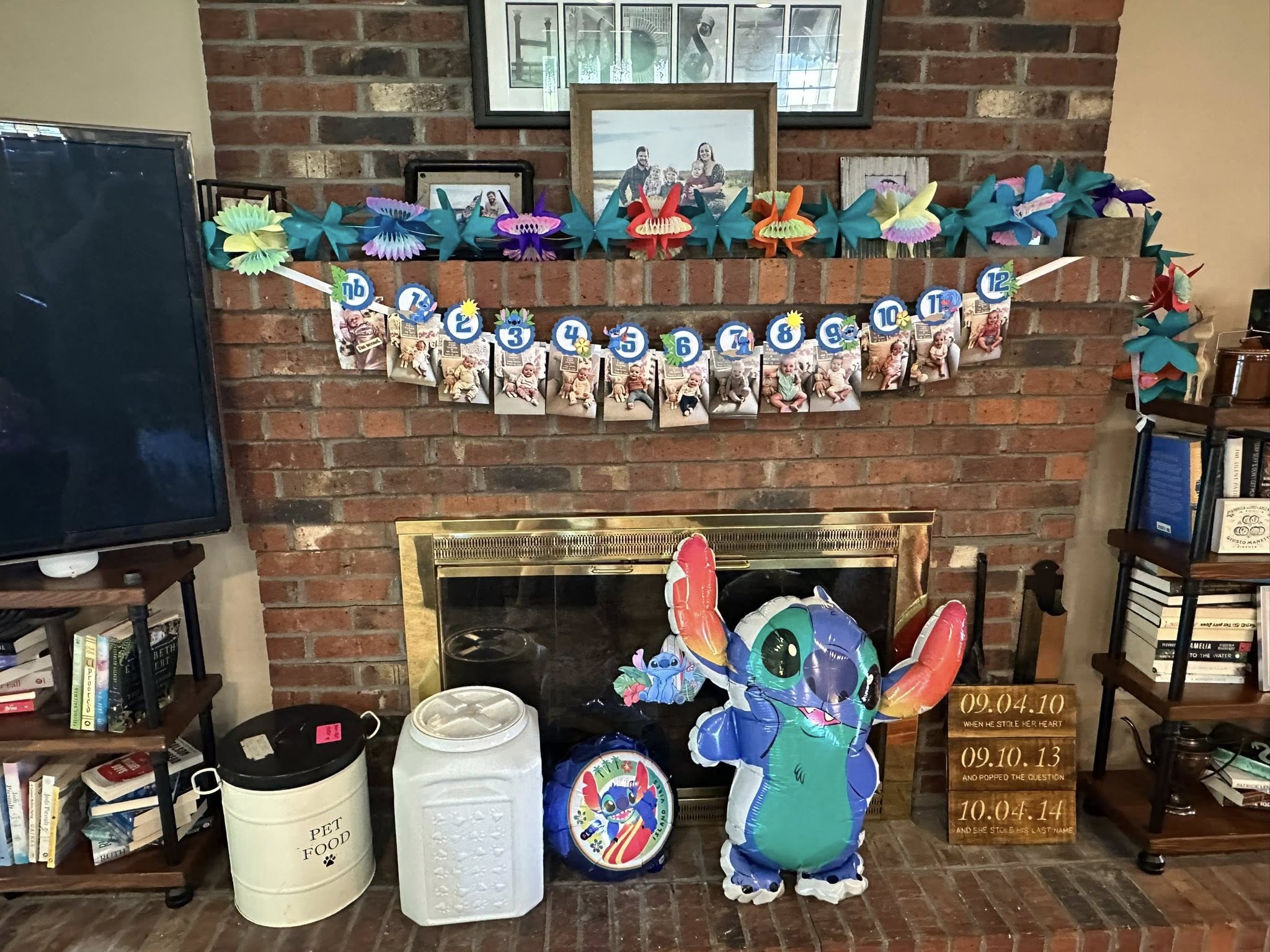 Stitch themed birthday decorations with monthly milestone photos hanging on a brick fireplace mantle.
