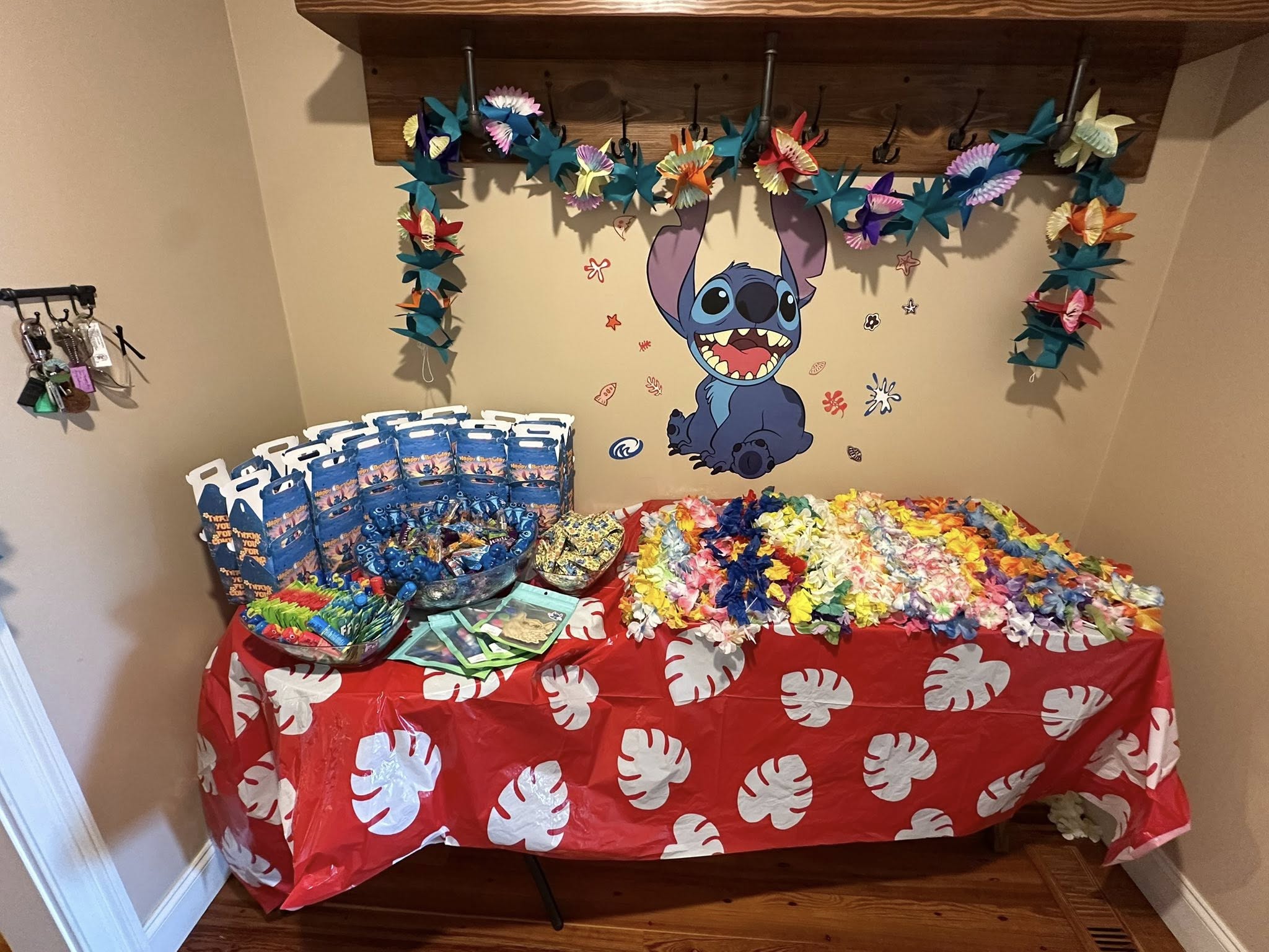 Stitch themed birthday party setup with treat bags, leis, and tropical decorations on a red monstera leaf tablecloth