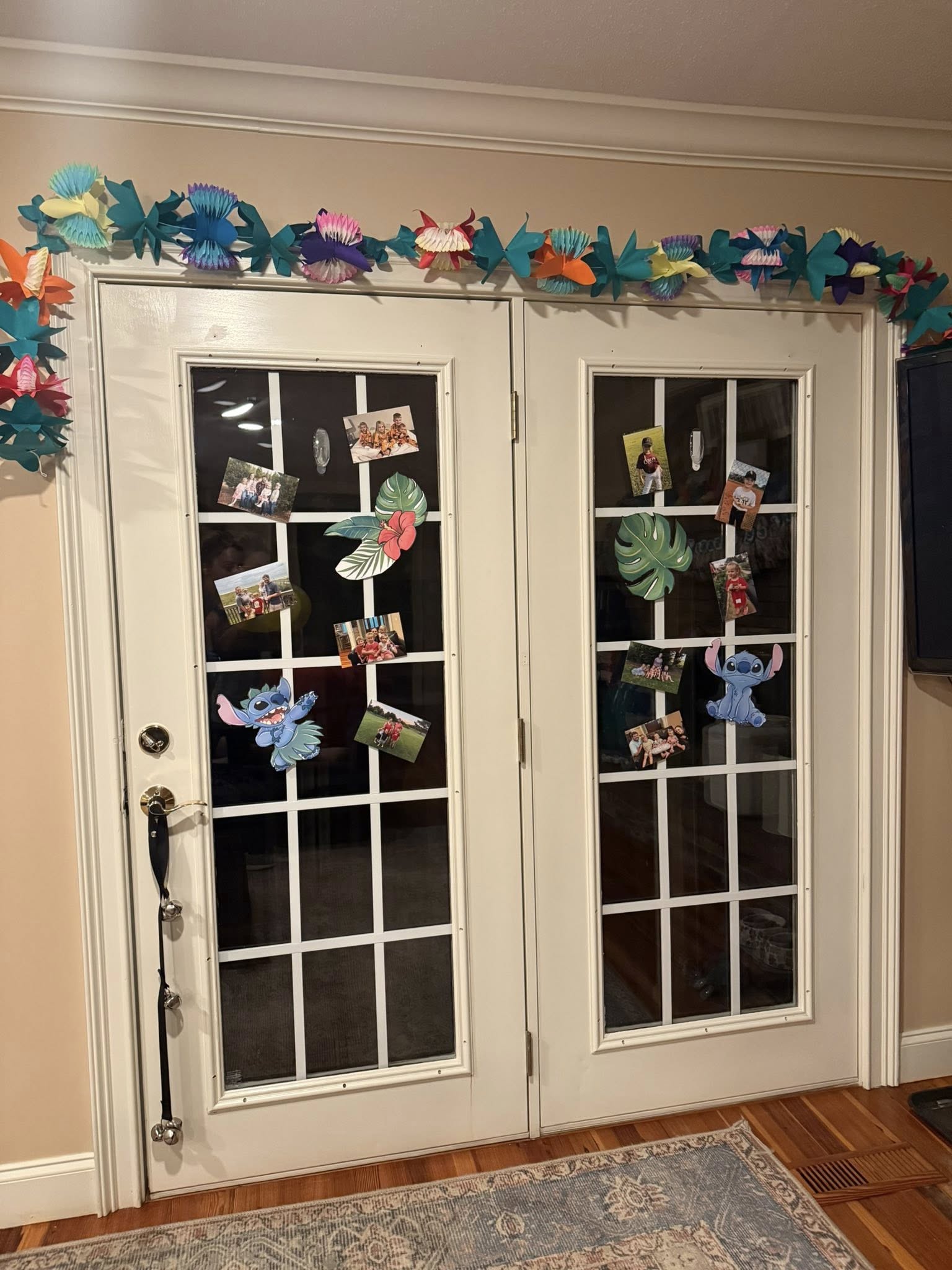 Double glass doors decorated with tropical paper flowers, Monstera leaves, and Stitch icons along with family photos.