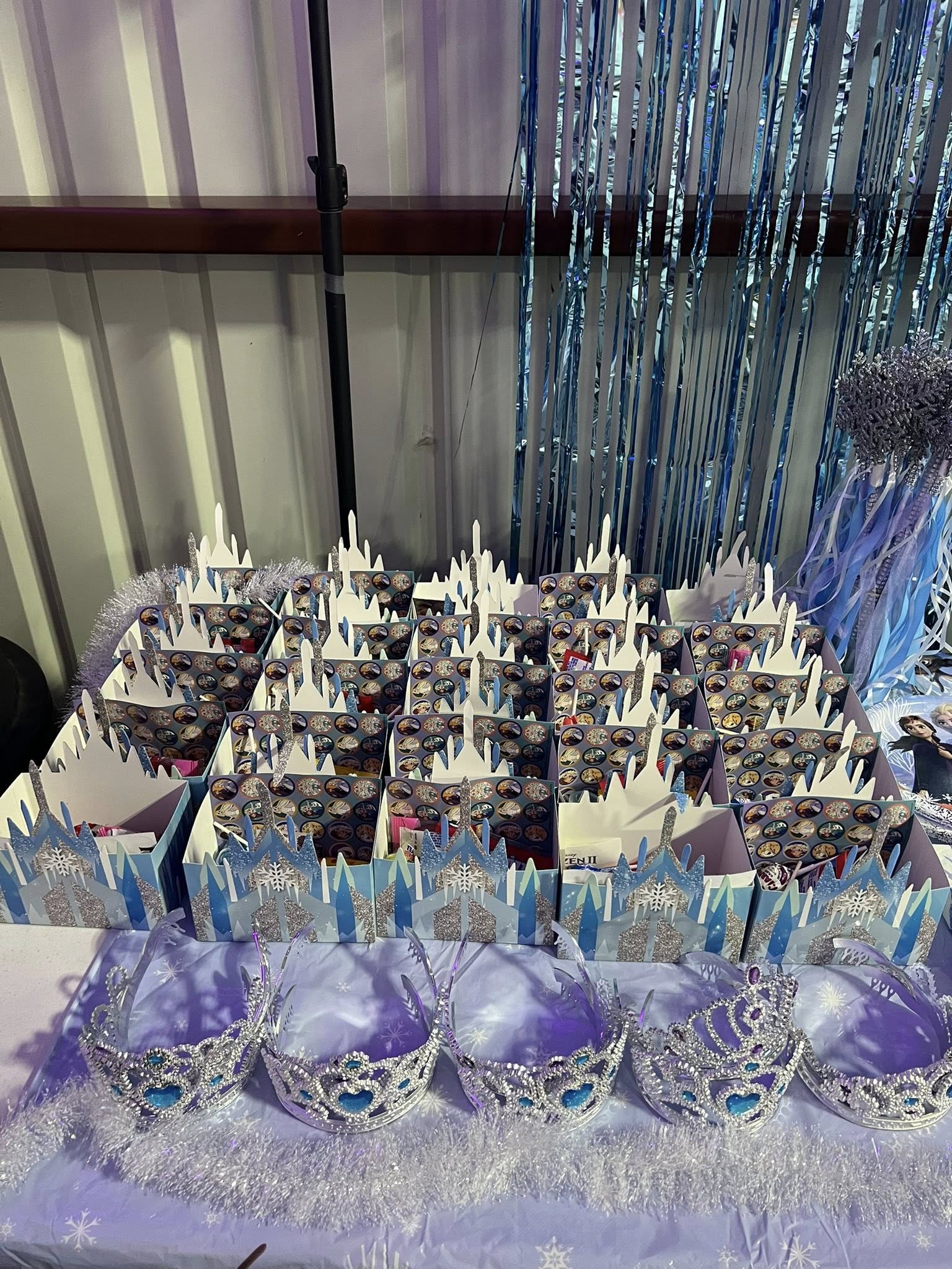 Frozen-themed party favor boxes shaped like ice castles with plastic tiaras arranged in the foreground