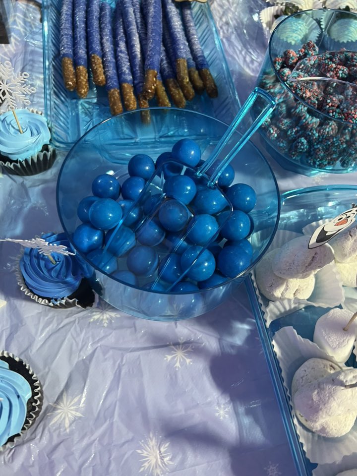 Table with blue gumballs, chocolate covered pretzels, and cupcakes, accented with Frozen themed decorations.