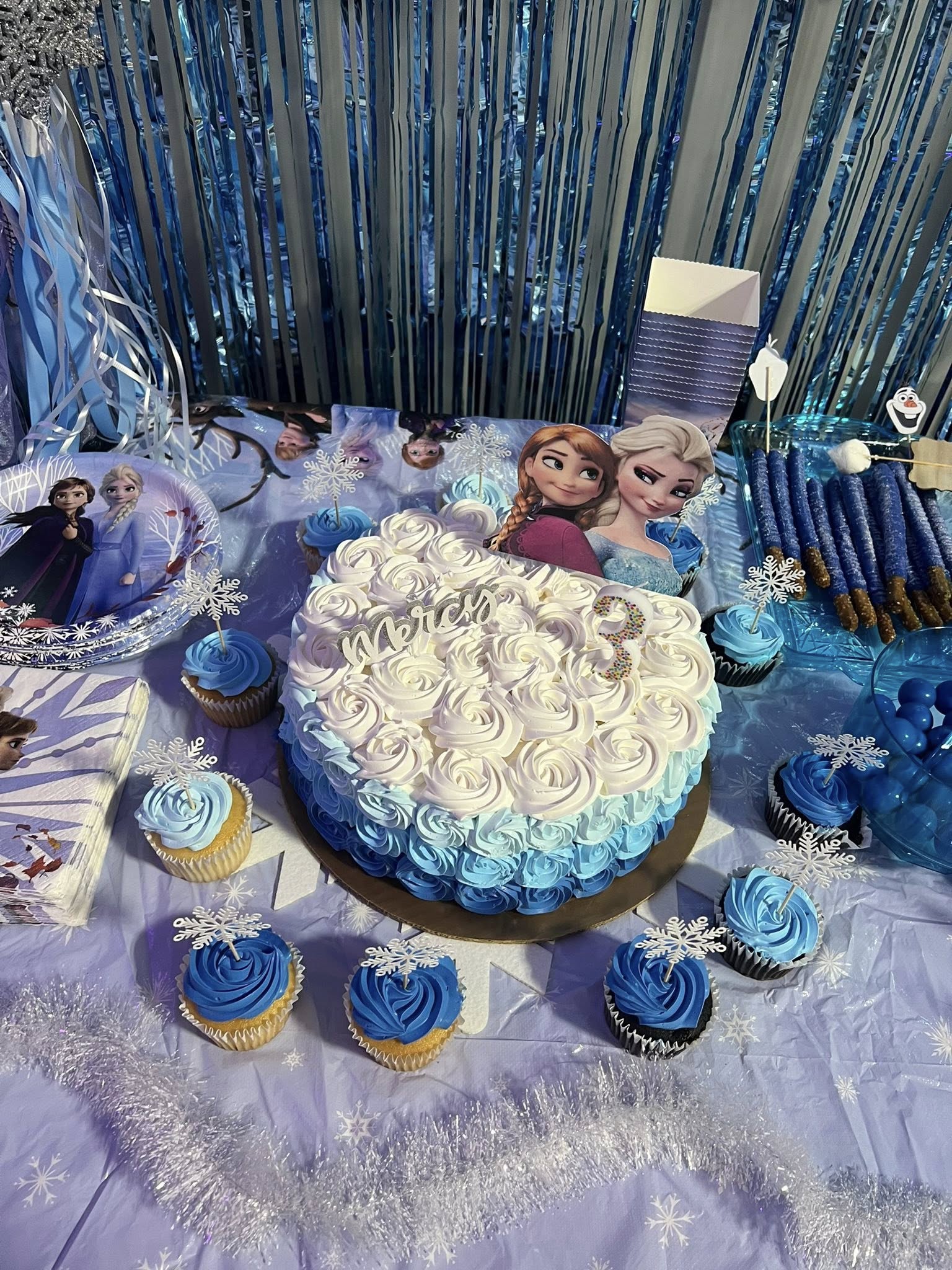 Frozen themed birthday cake with blue and white ombre rosettes and Anna and Elsa cake toppers.