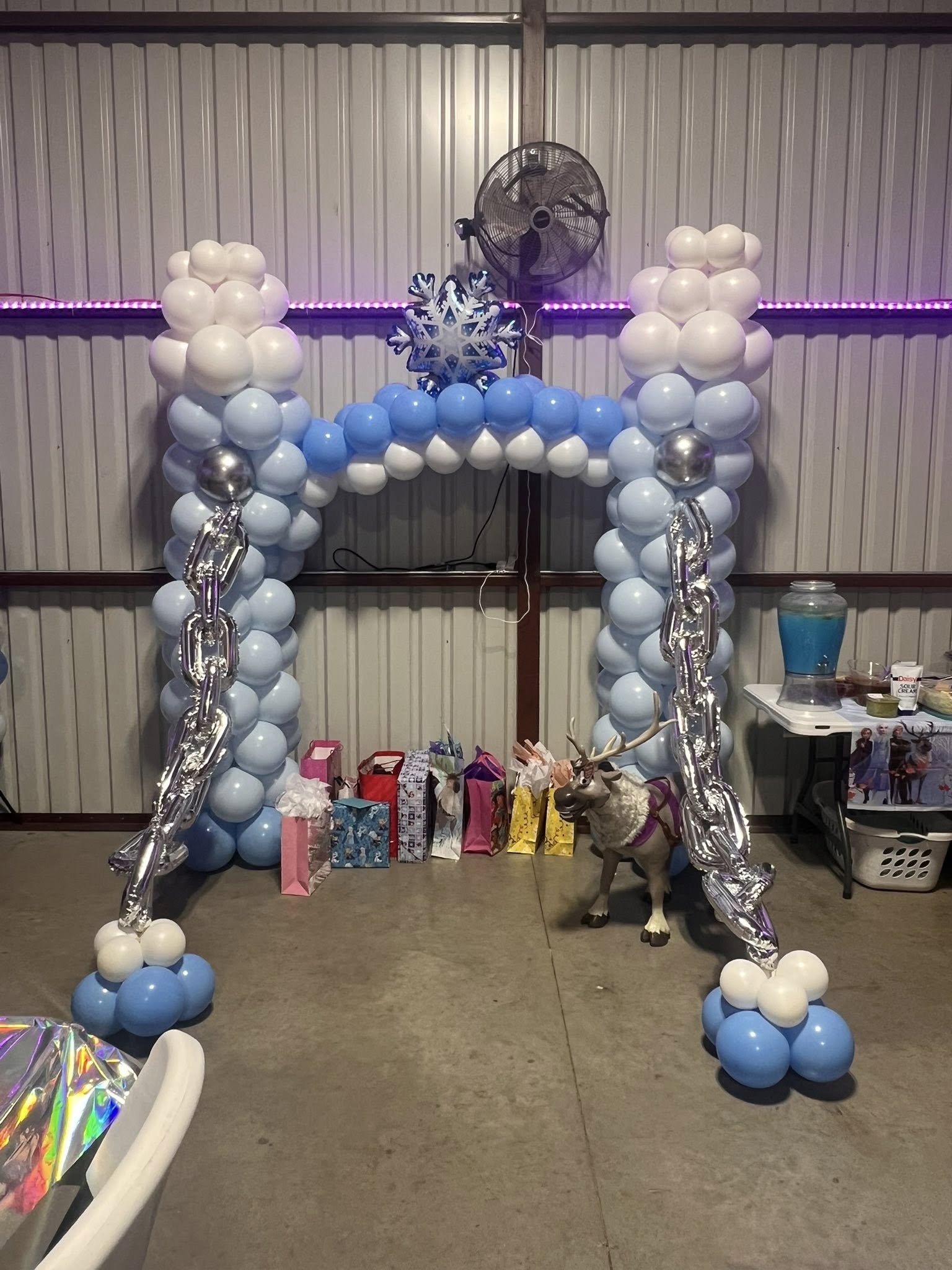 Frozen-themed balloon arch with a snowflake topper and silver foil chains in front of gift bags