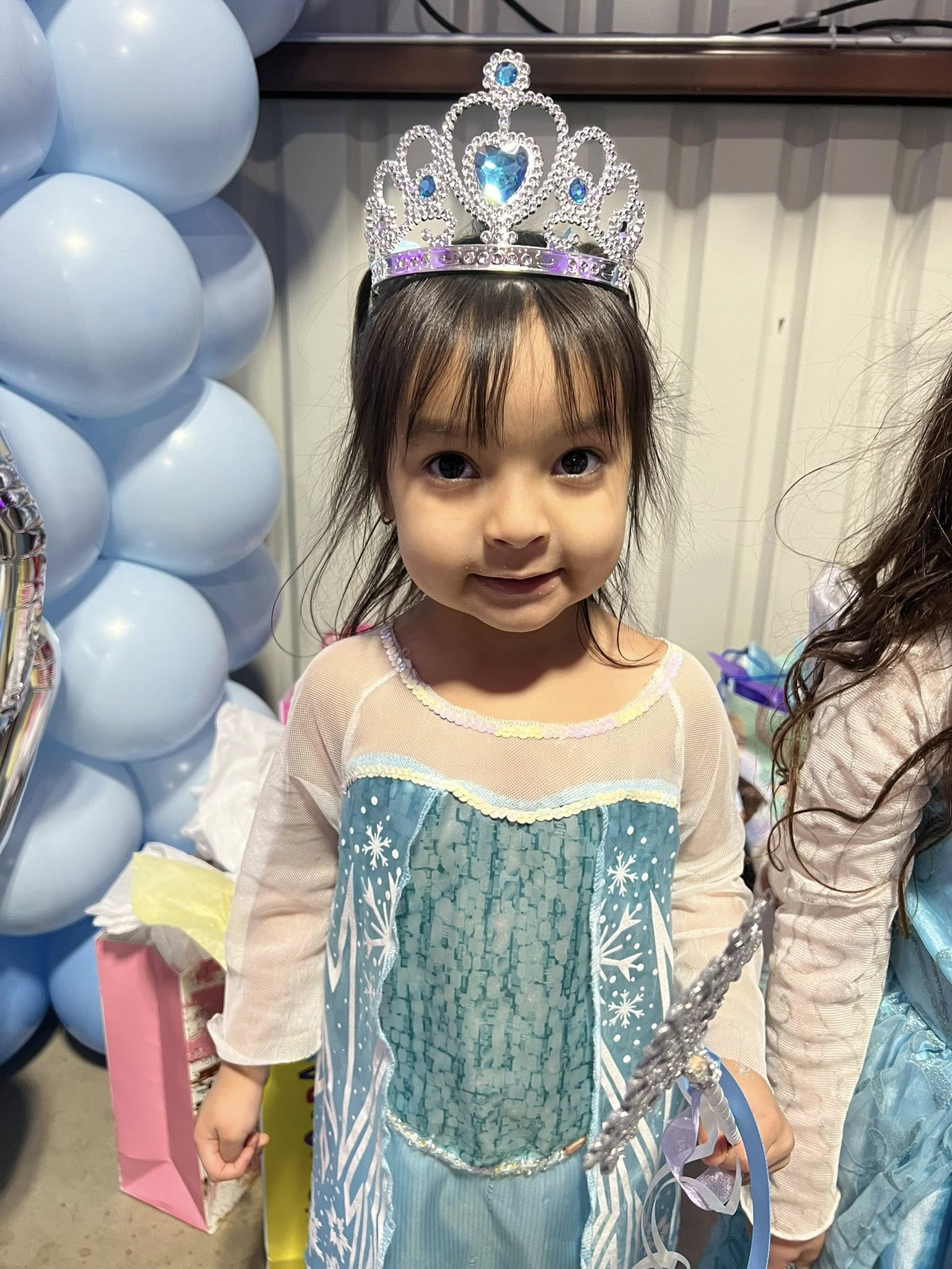 Young girl smiling while wearing a sparkly blue princess dress and a rhinestone tiara