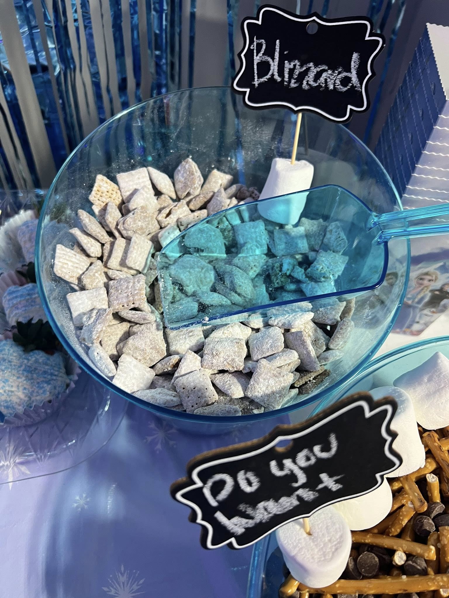 Bowl of Blizzard snack mix with a blue scoop and a label, served at a winter-themed party.